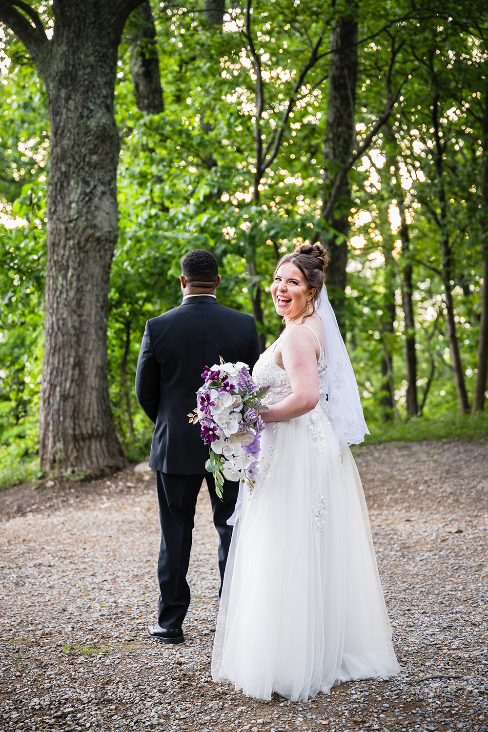 A bride smiles widely as she looks over her shoulder to pose for a quick photo before tapping her partner on the shoulder for their first look at Mill Mountain Park in Roanoke, Virginia on their wedding day.