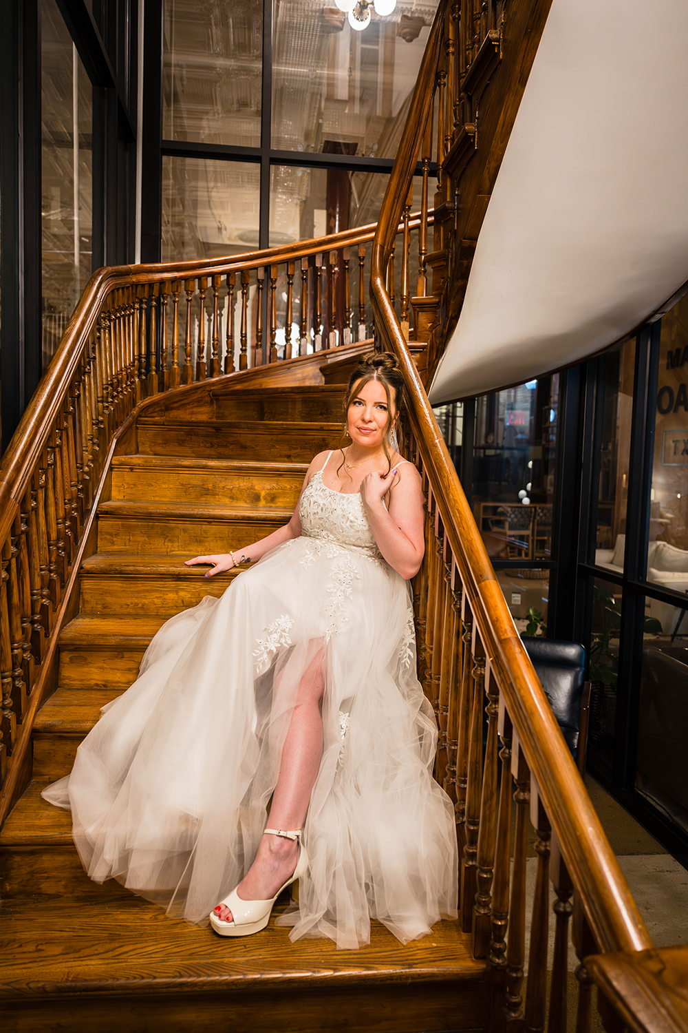 A woman wearing a wedding dress sits and poses on the antique stairwell at Fire Station One Boutique Hotel in Roanoke, Virginia.