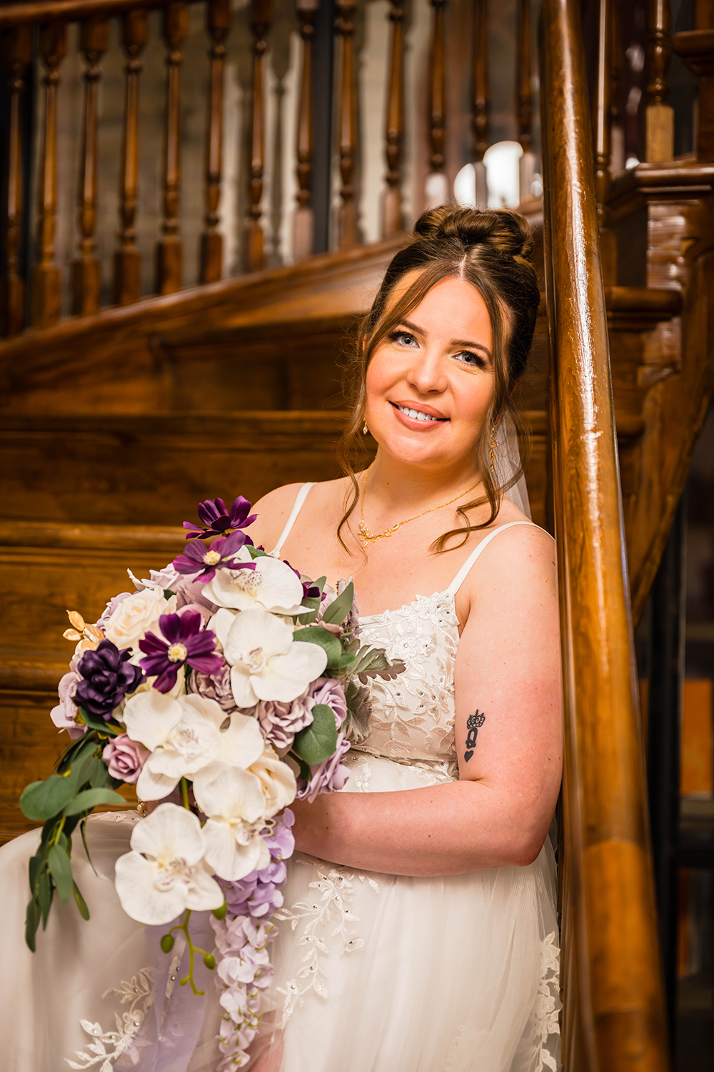 A bride sits on the stairs of the Fire Station One Boutique Hotel in Roanoke, Virginia and smiles as she leans her head against the handrail and holds her bouquet in her lap.