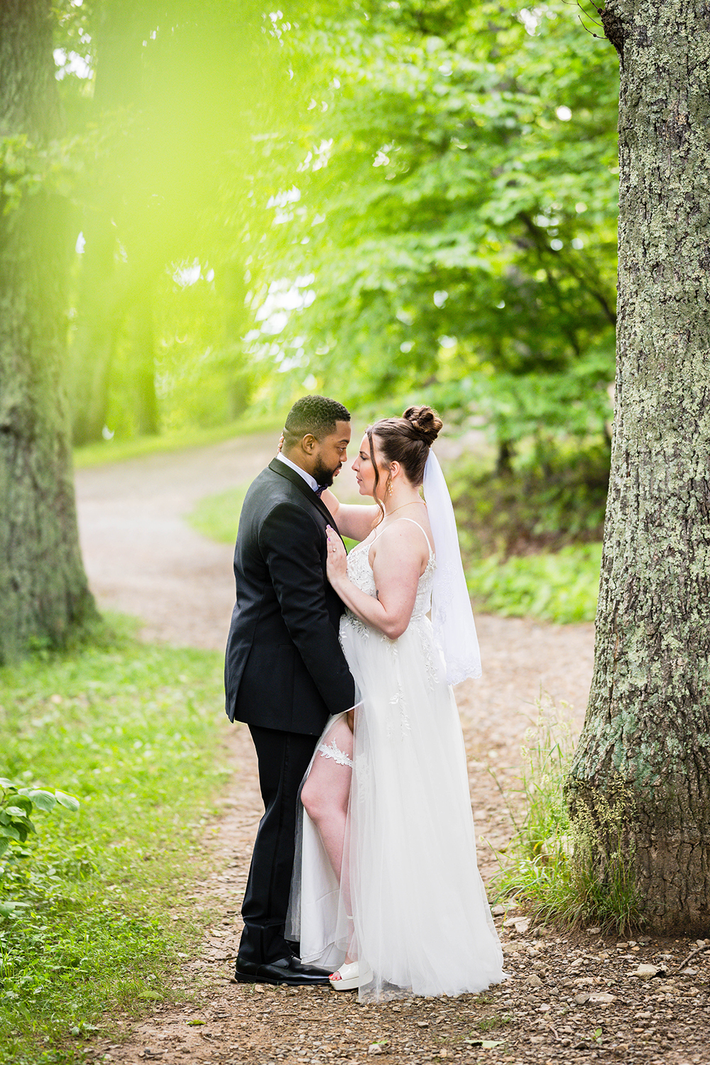 Two marriers look seductively at one another at Mill Mountain Park on their wedding day. A marrier wearing a wedding dress is showing her leg from under a slit in her dress to expose a garter and her partner has placed his hand on her upper thigh just above the garter.