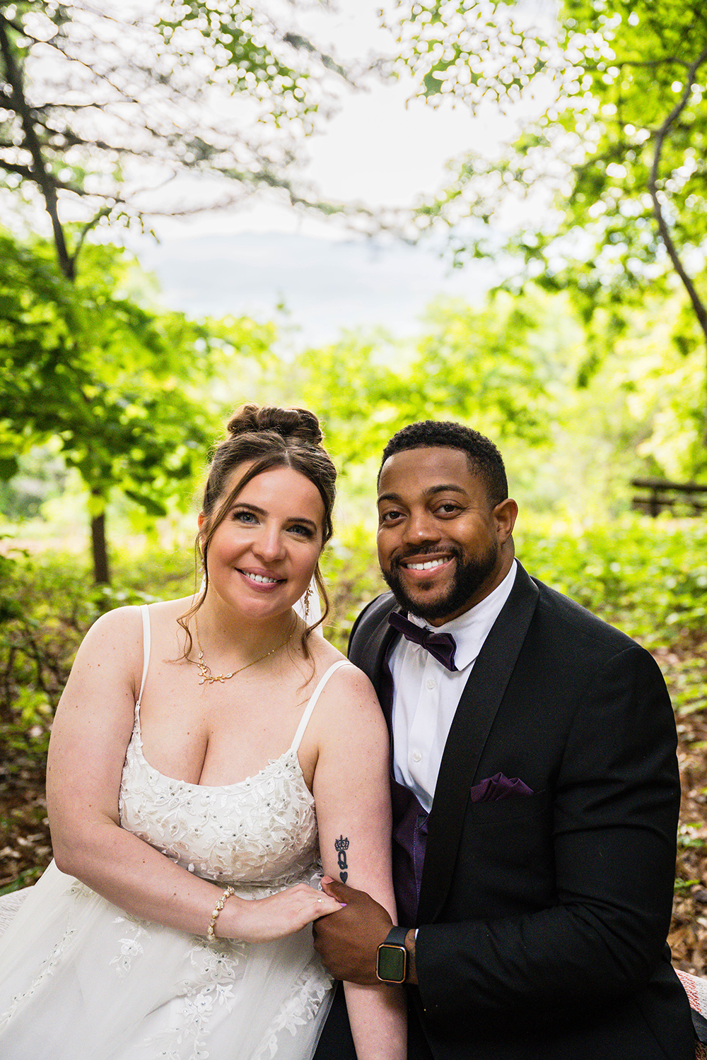 A couple on their elopement day sit on a bench and smile for a quick photo before eating their breakfast picnic at the Mill Mountain Wildflower Garden in Roanoke, Virginia.