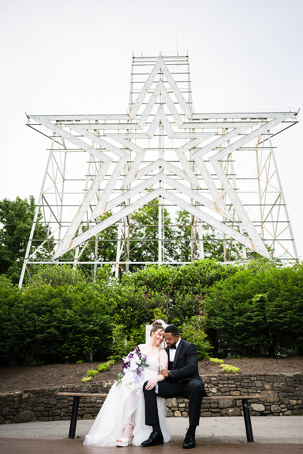 A couple on their wedding day sits on a bench and poses for a photo in front of the iconic Roanoke Star at Mill Mountain Park in Southwest Virginia.