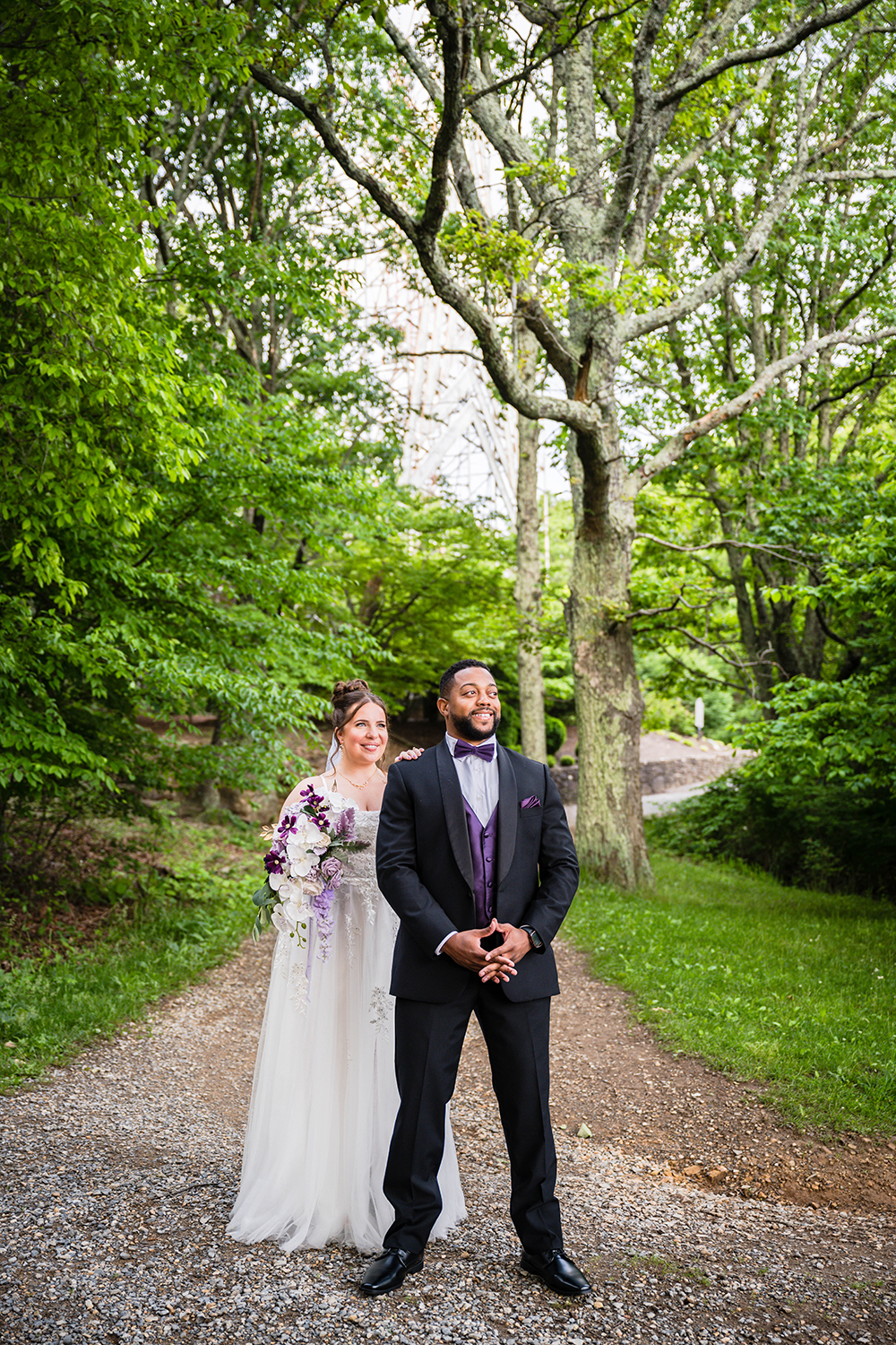 A marrier smiles as she goes to tap her partner's shoulder during their first look at Mill Mountain Park. Her partner, who is standing in front of her, smiles widely and waits in anticipation.