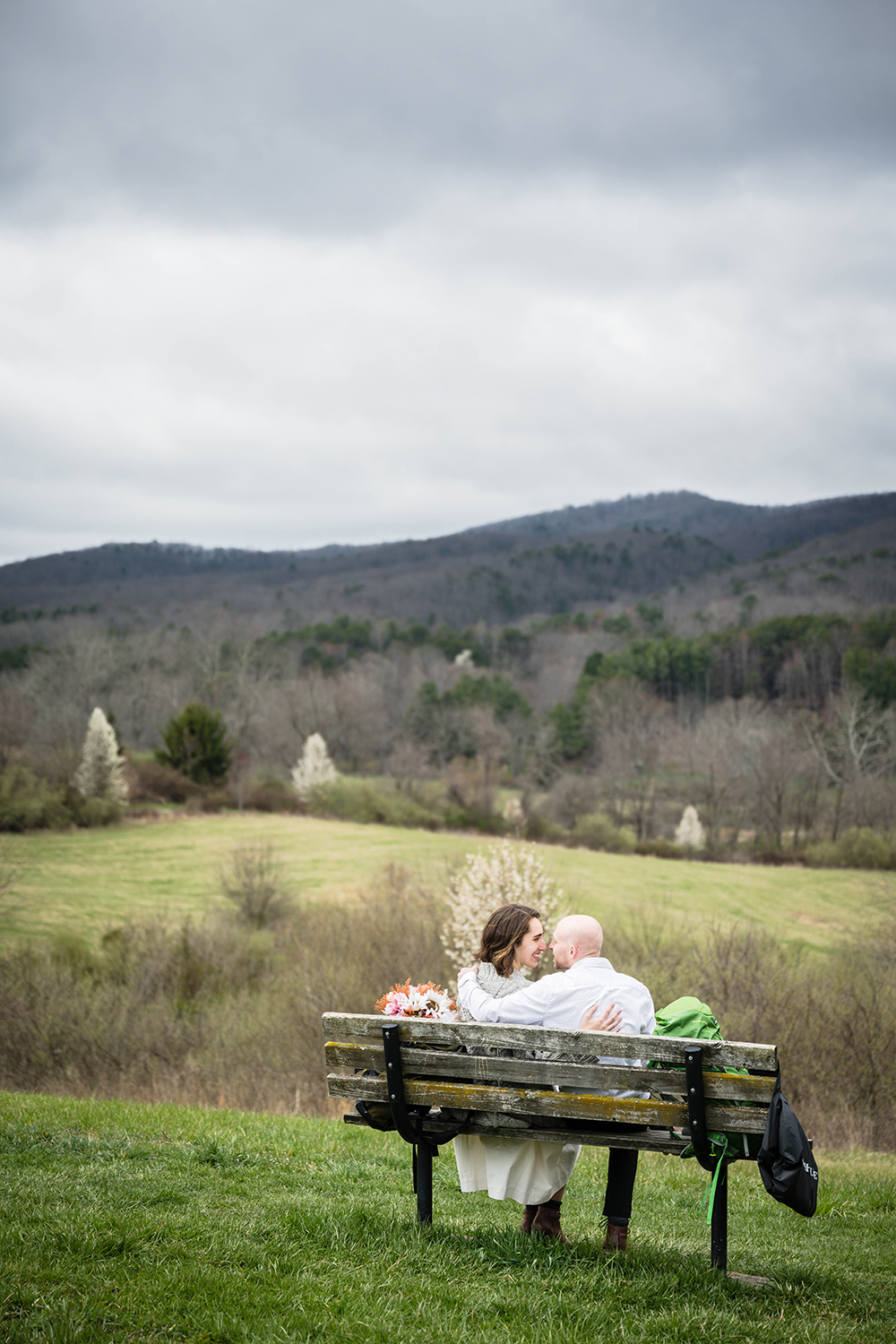 A couple sit on a bench along a trail on the Blue Ridge Parkway in Virginia on their elopement day. 