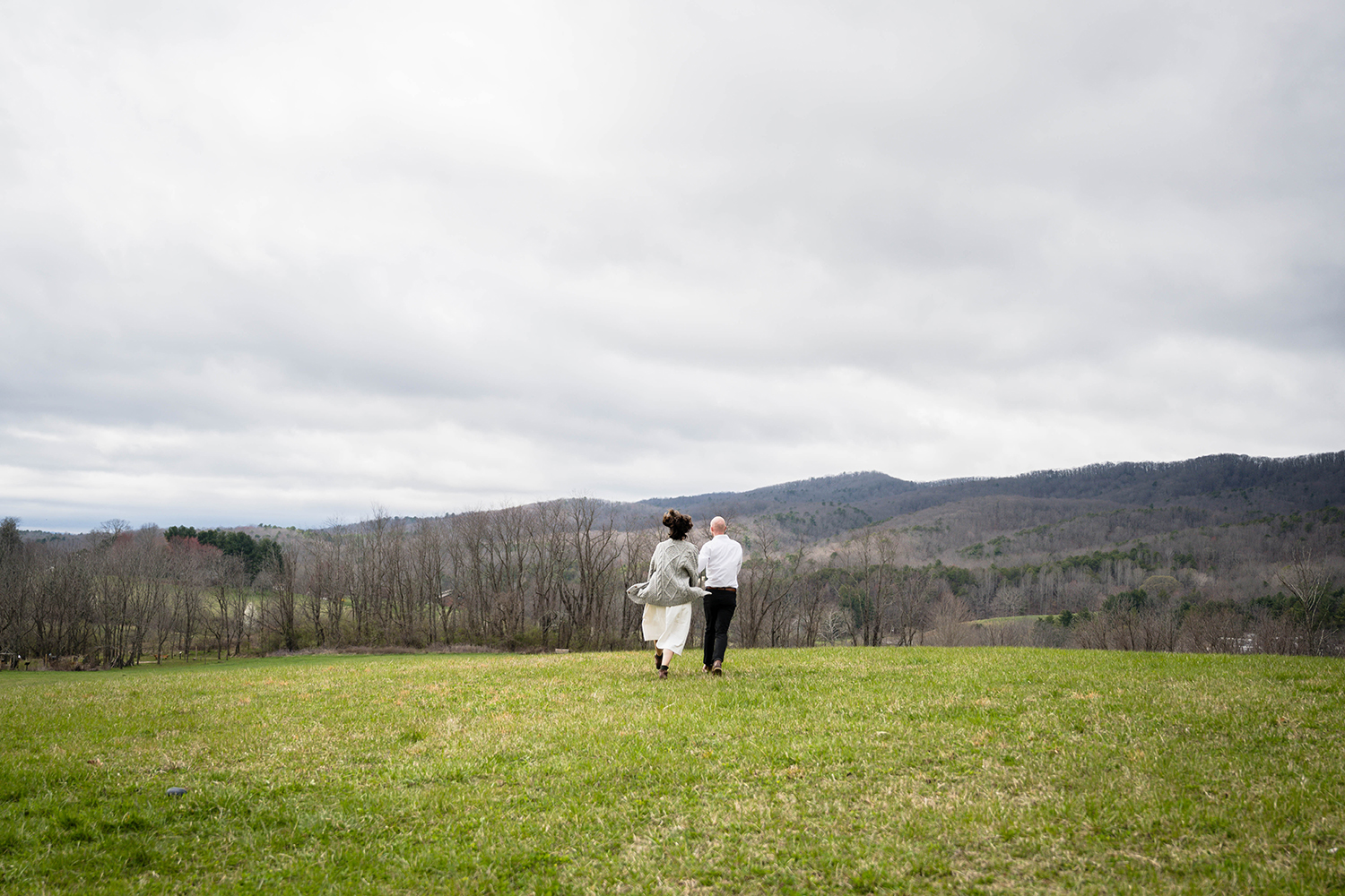 A couple runs towards the mountains hand-in-hand on their elopement day in the Blue Ridge Parkway in Virginia.