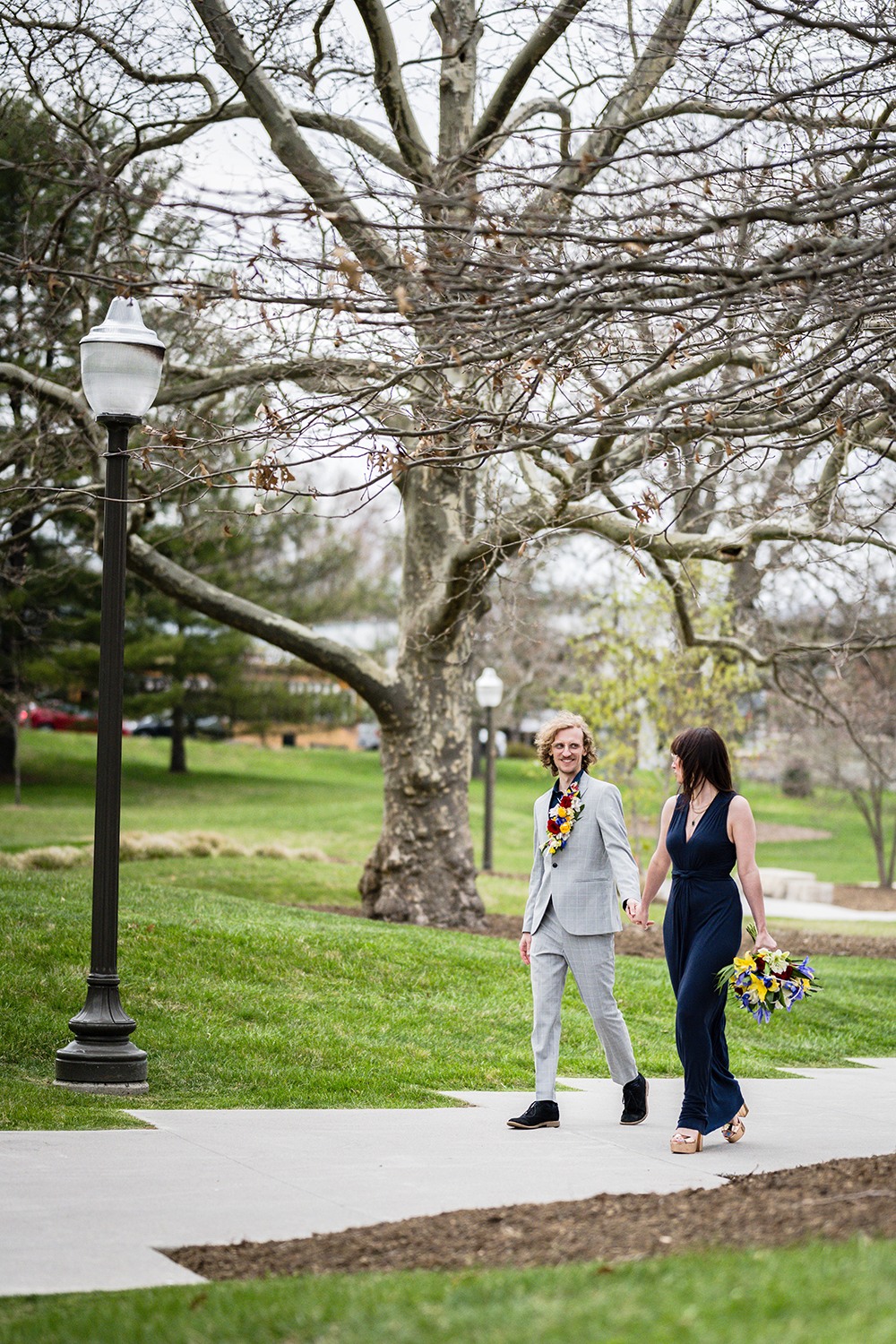 A couple walk hand-in-hand under a tree with many branches on Virginia Tech's campus on their intimate wedding day.