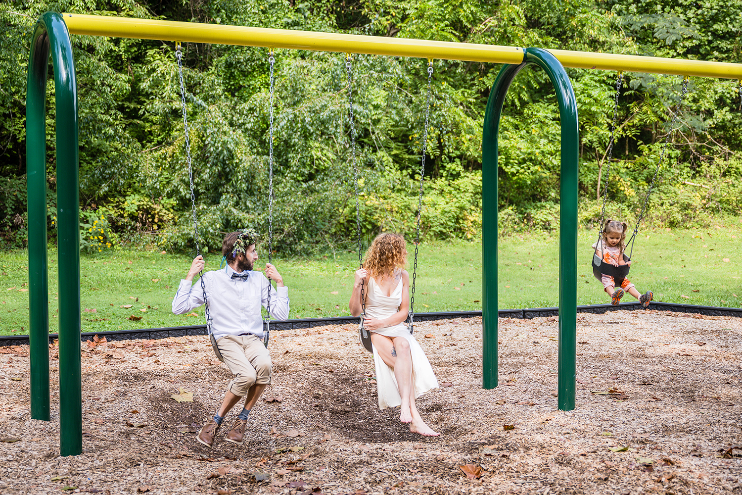 A couple on their elopement day swing alongside their daughter at Fishburn Park in Roanoke, Virginia.