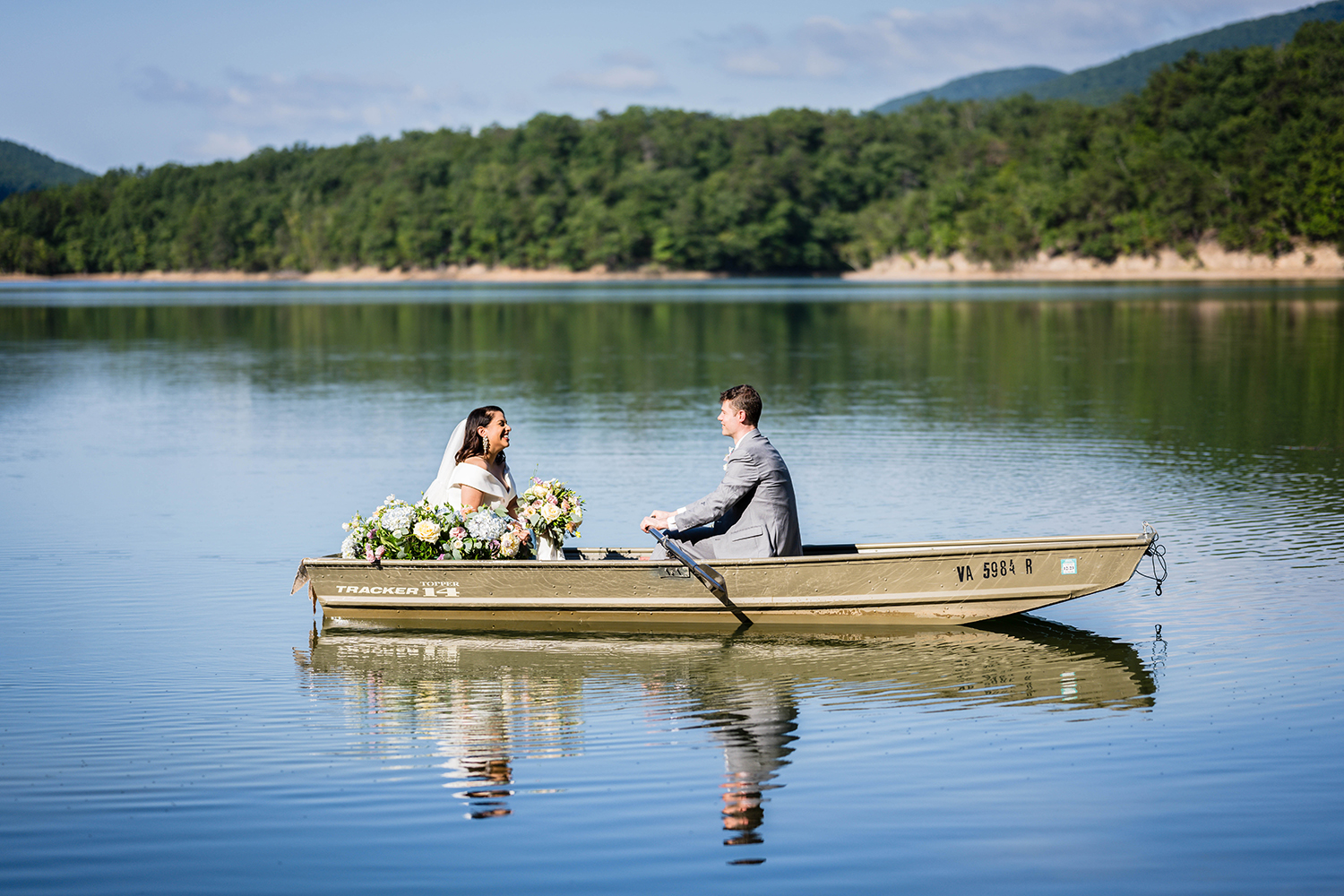 A couple sits in a rowboat in the waters of Carvin's Cove and smile at one another.