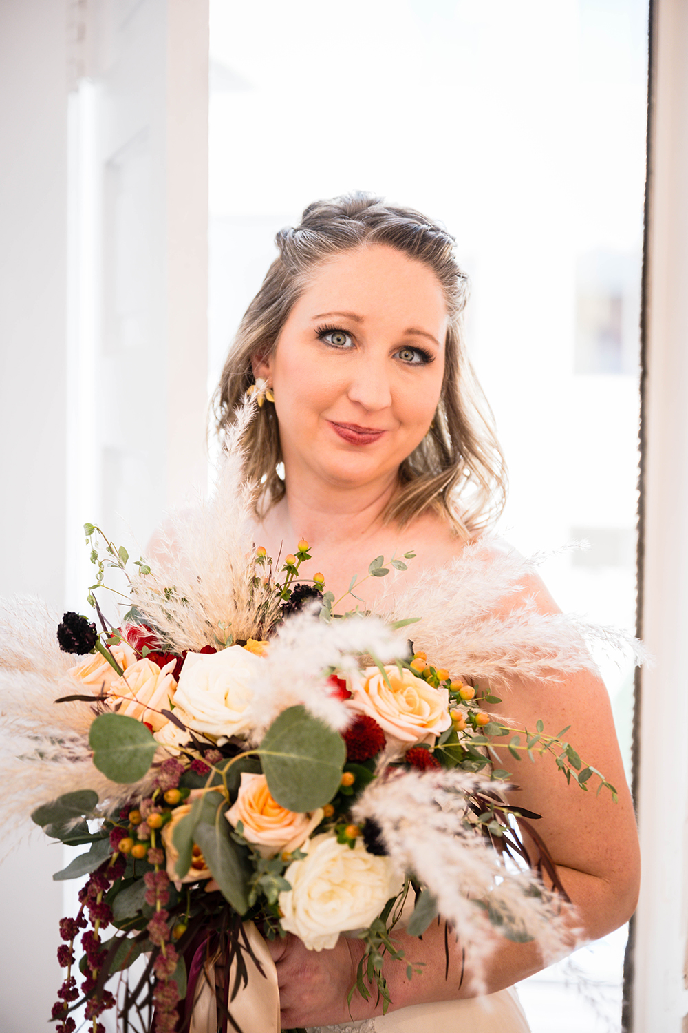 A bride holds a bouquet close to her chest inside her hotel room at Fire Station One in Downtown Roanoke and looks to the camera for a photo. 