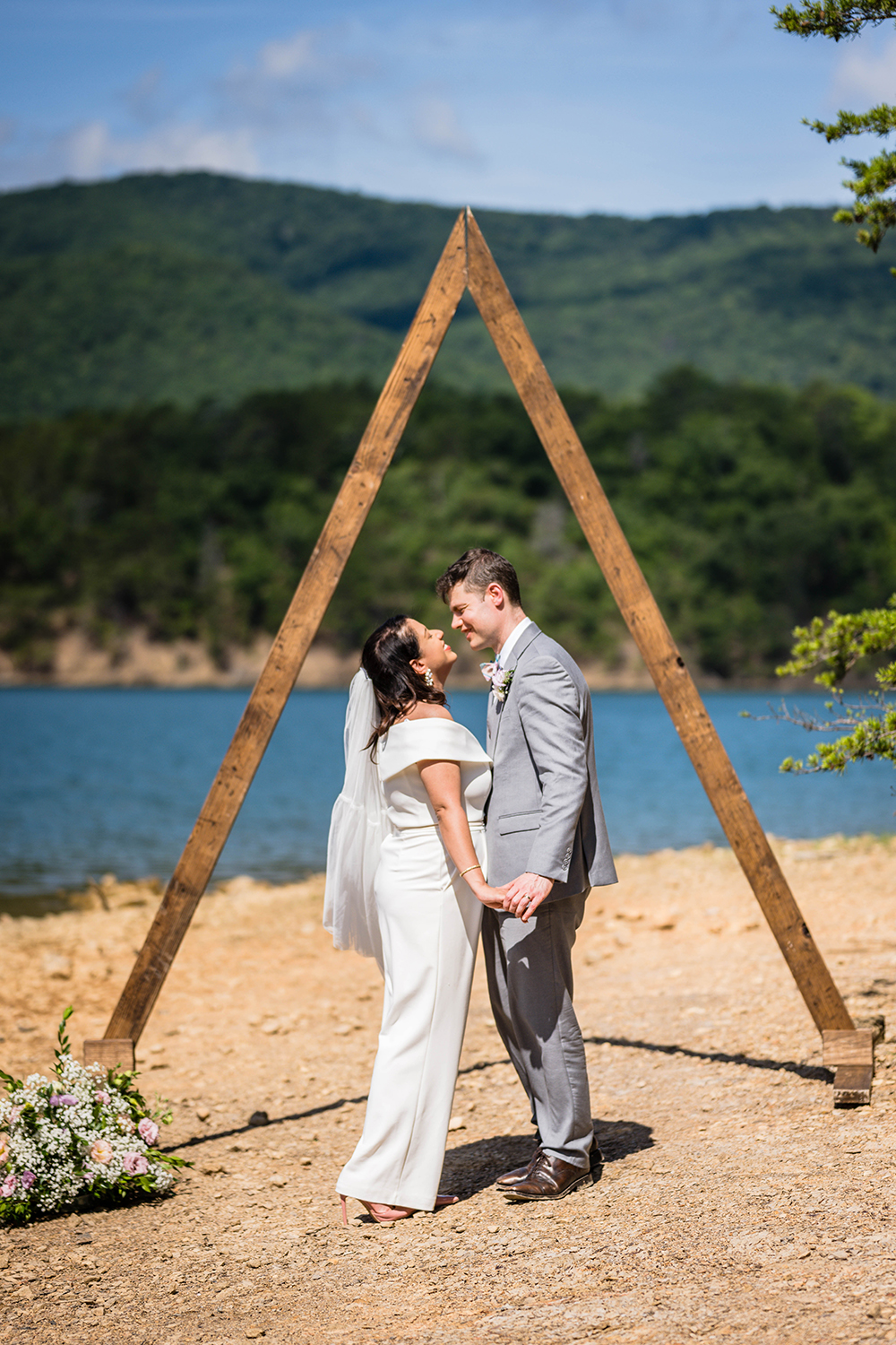 A couple goes for a kiss under a triangle arch adorned with flowers at Carvin's Cove during their elopement in Roanoke, VA.