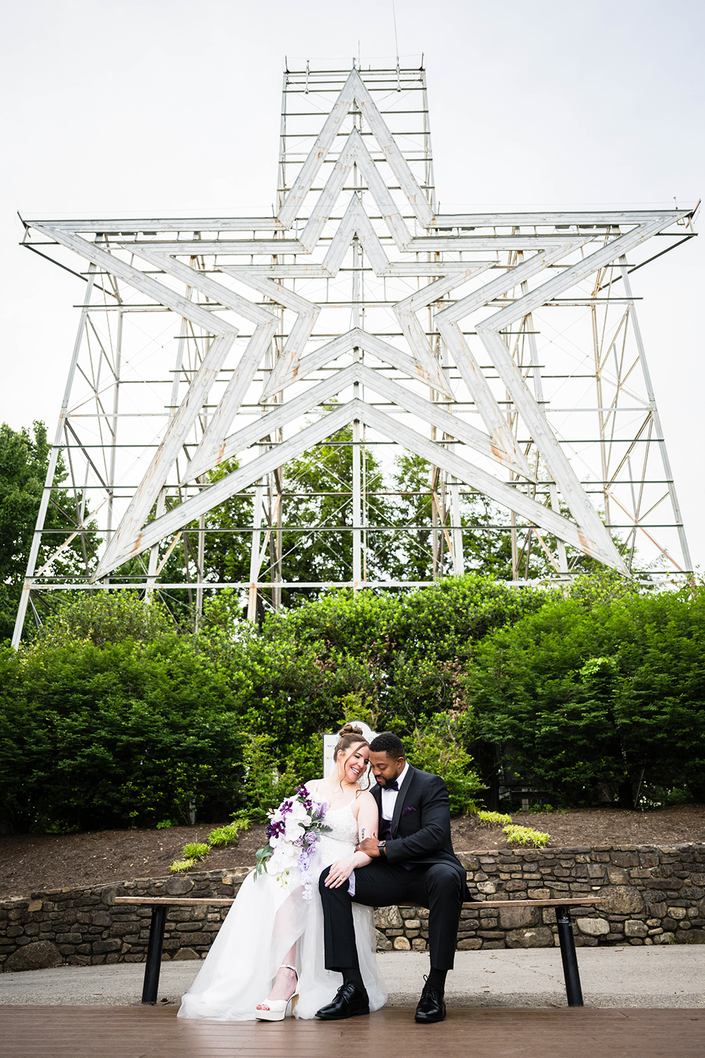 A couple sits on a bench and poses in front of the Mill Mountain Star during their elopement in Roanoke, VA.