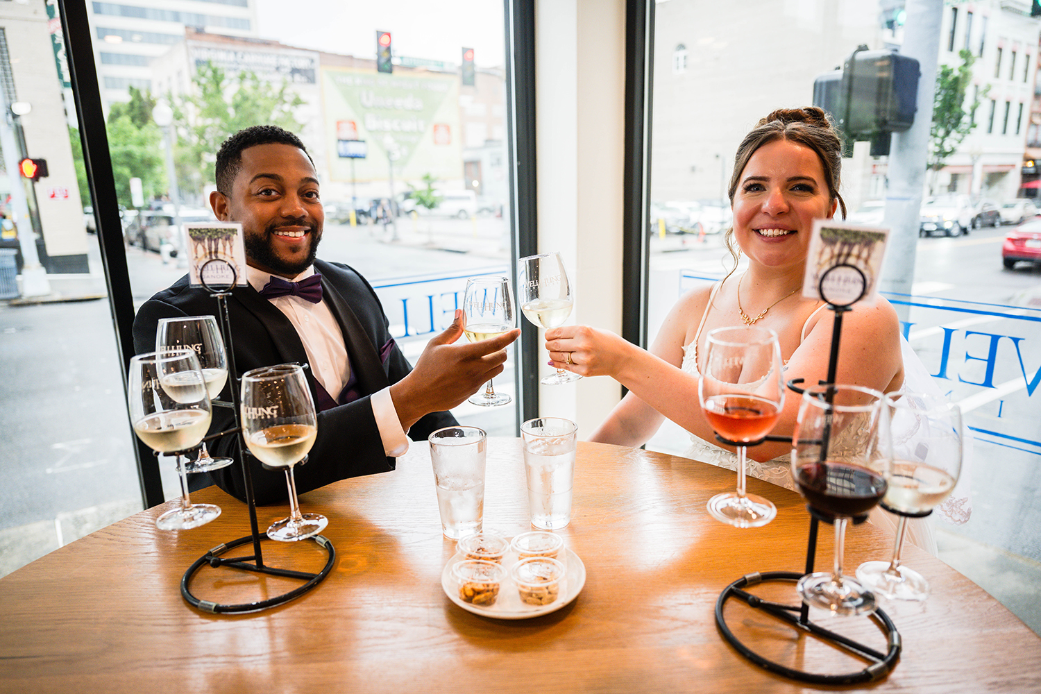 A couple sits at a table and clinks their wine glasses together as they enjoy a tasting at Wellhung Vineyard in Downtown Roanoke on their elopement day.