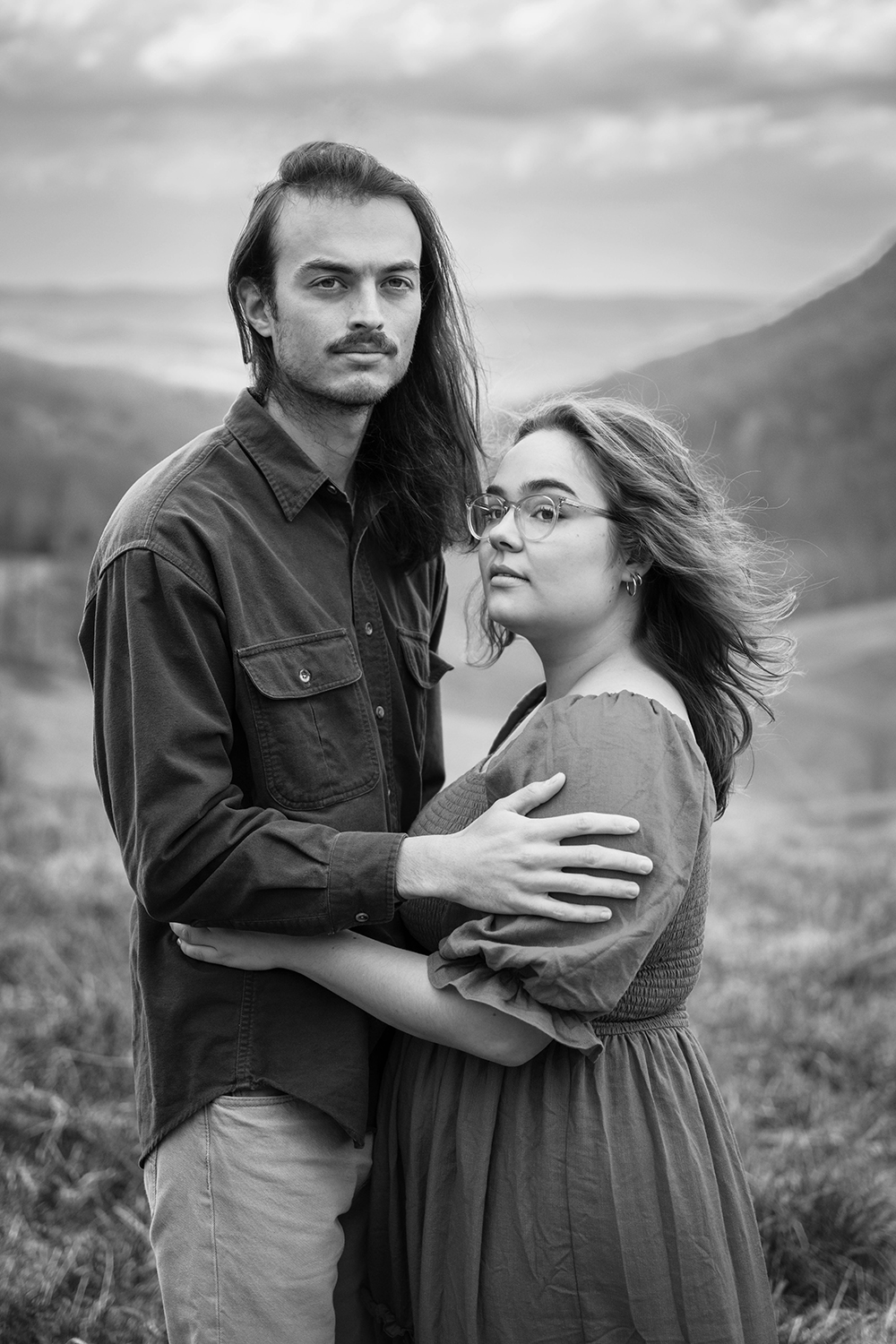 A couple wraps their arms around one another as they each look off into the distance during their anniversary adventure session at Hidden Hills in Giles County, Virginia.