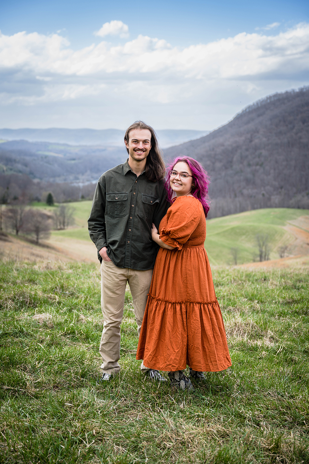 A couple wraps their arms around one another and smiles for a photo during their anniversary adventure session at Hidden Hills in Giles County, Virginia.