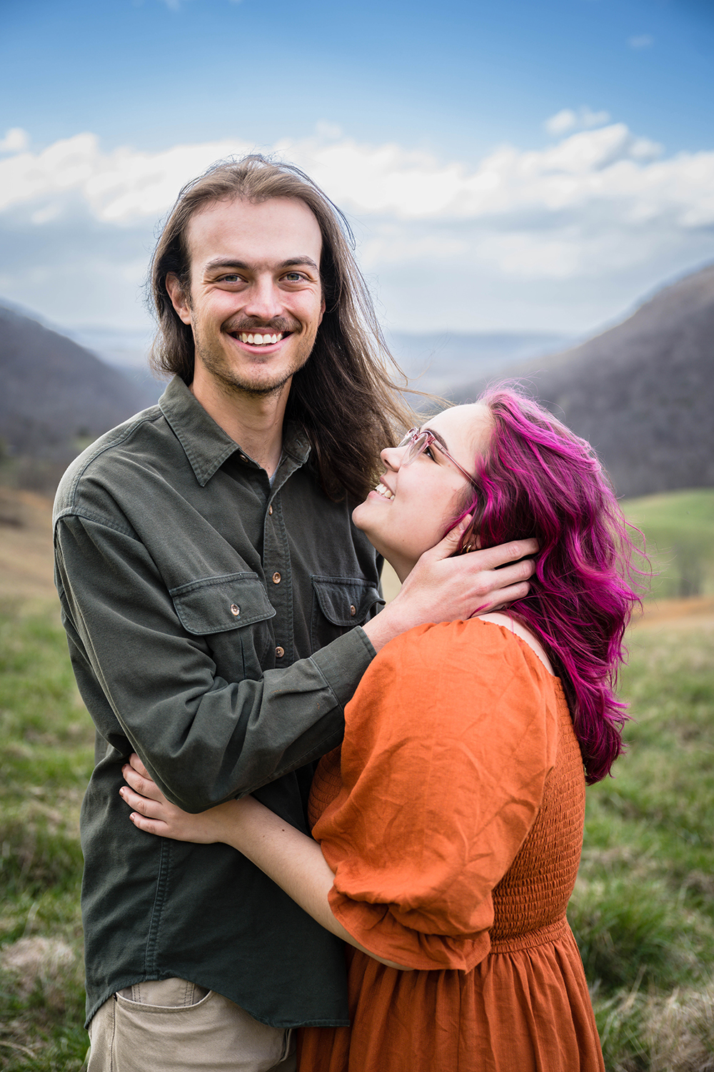 A woman wraps her arms around her significant other's waist and looks up as he smiles at the camera while holding her face during their anniversary photo session at Hidden Hills in Giles County, Virginia.