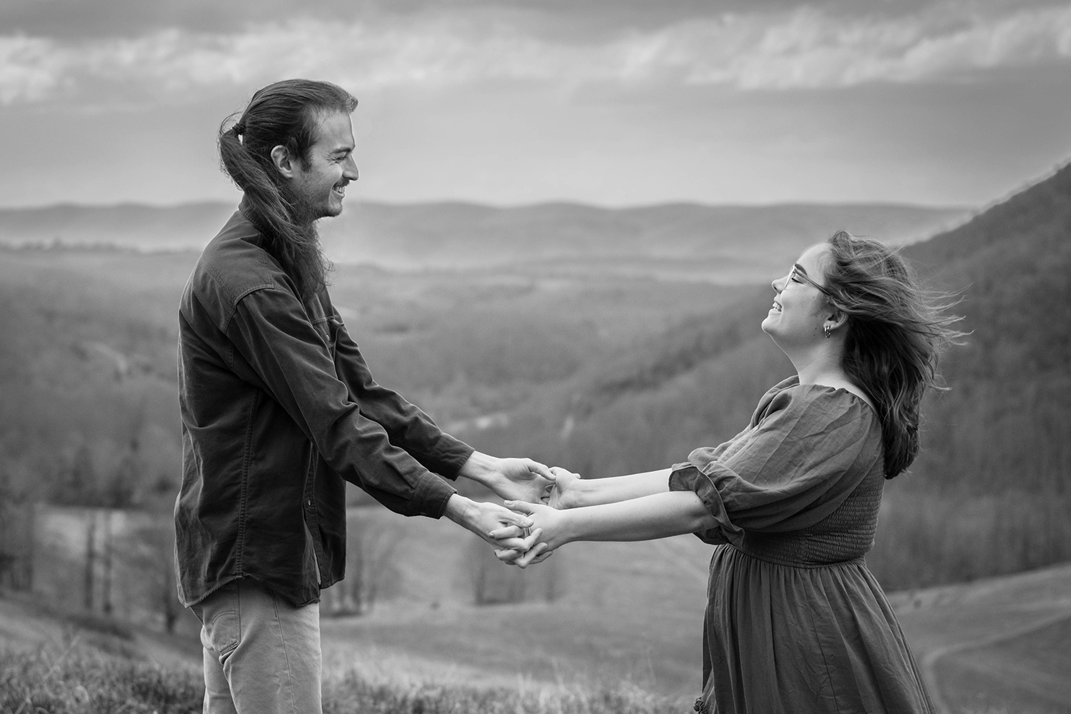 A couple hold hands while facing one another and smiling during their anniversary photo session in Giles County, Virginia. The photo is edited with a black and white filter.