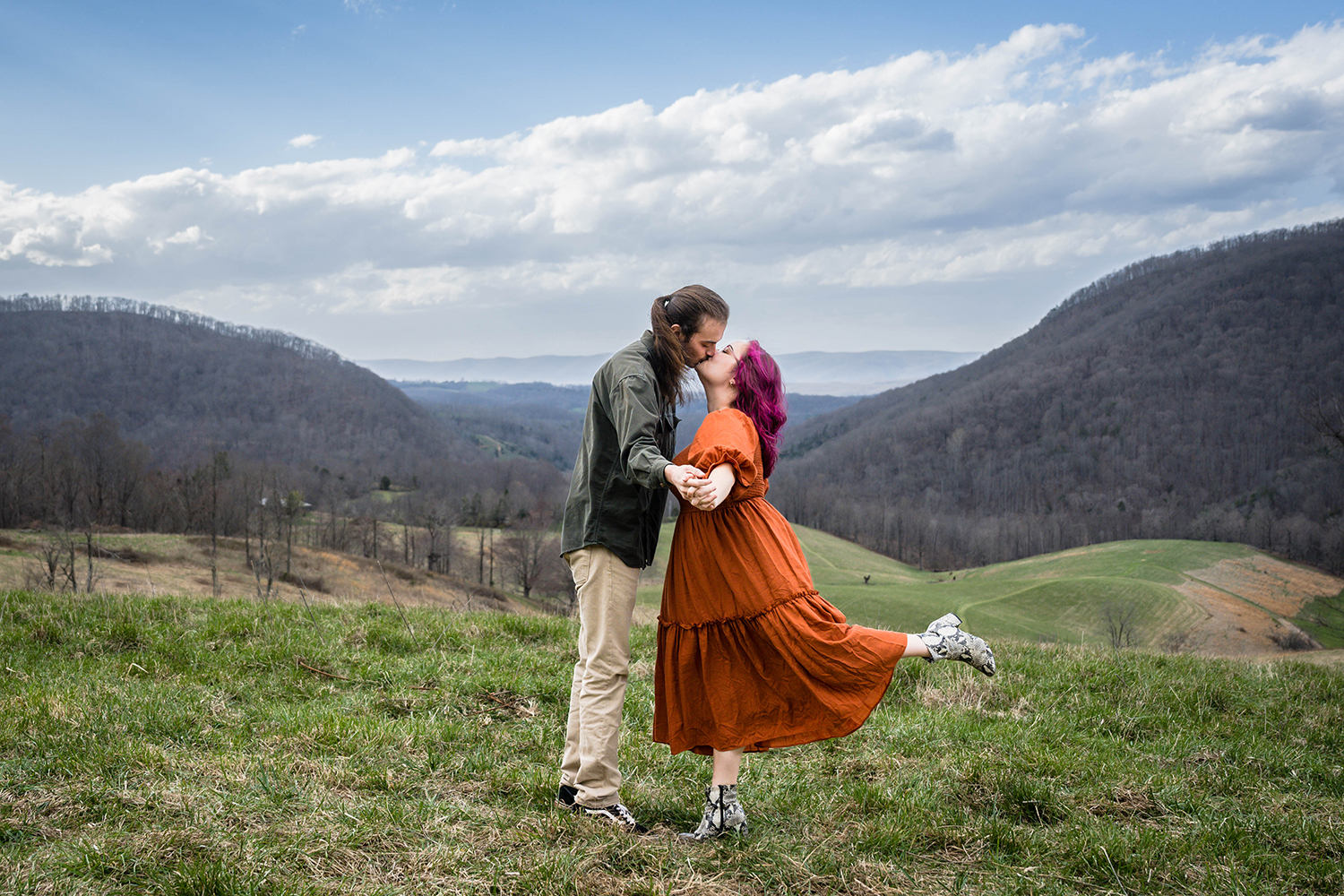 A couple holds hands and sway into a kiss. The man keeps both feet planted on the ground while the woman lifts her leg upon impact. 