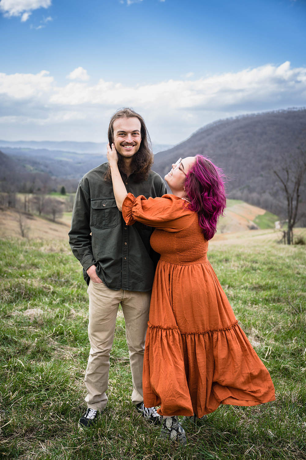 A woman turns towards her partner and holds onto his face and looks up at him smiling while he looks away and smiles.