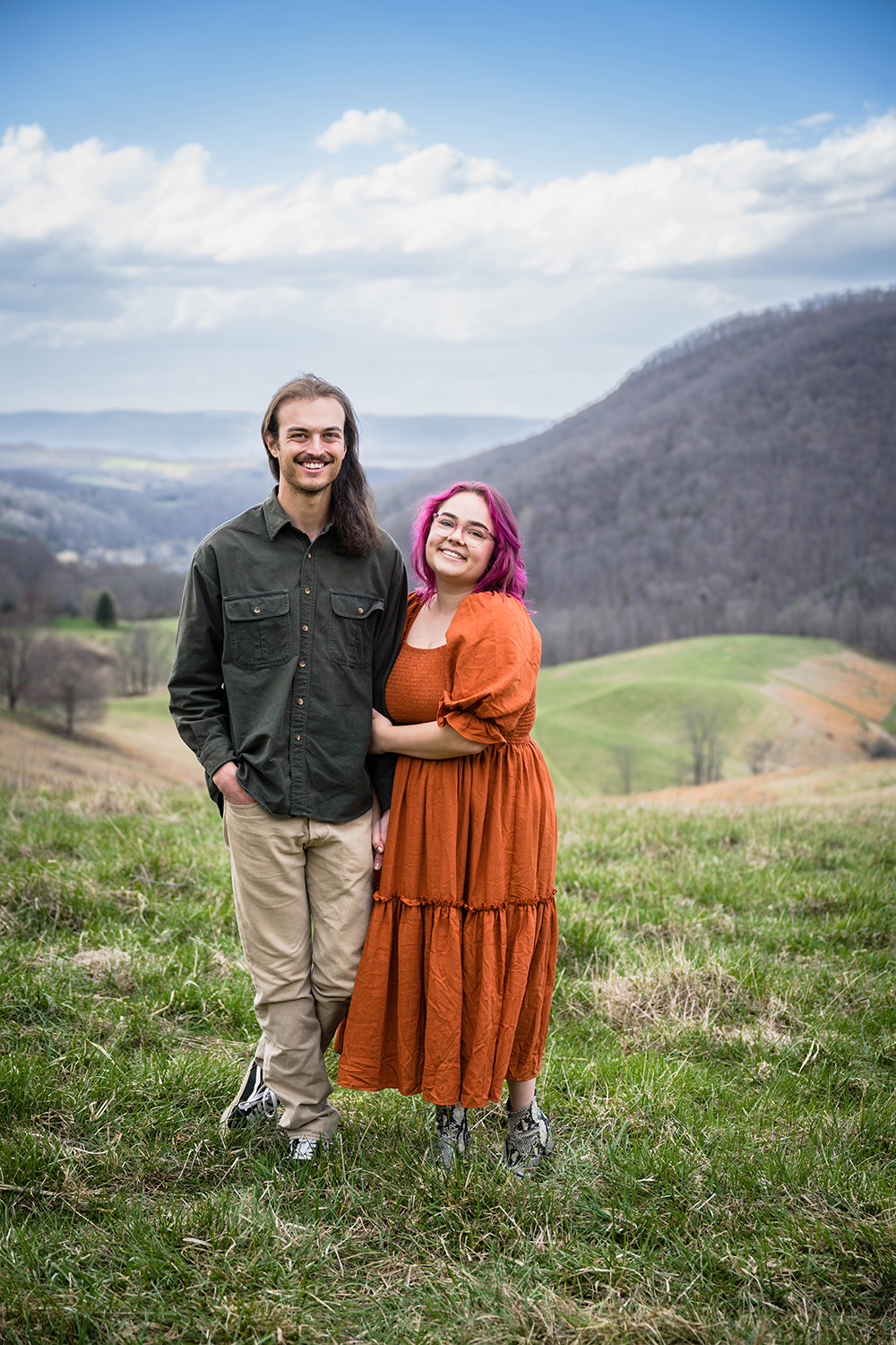 A couple wraps their arms around one another and smiles for a photo during their anniversary adventure session at Hidden Hills in Giles County, Virginia.