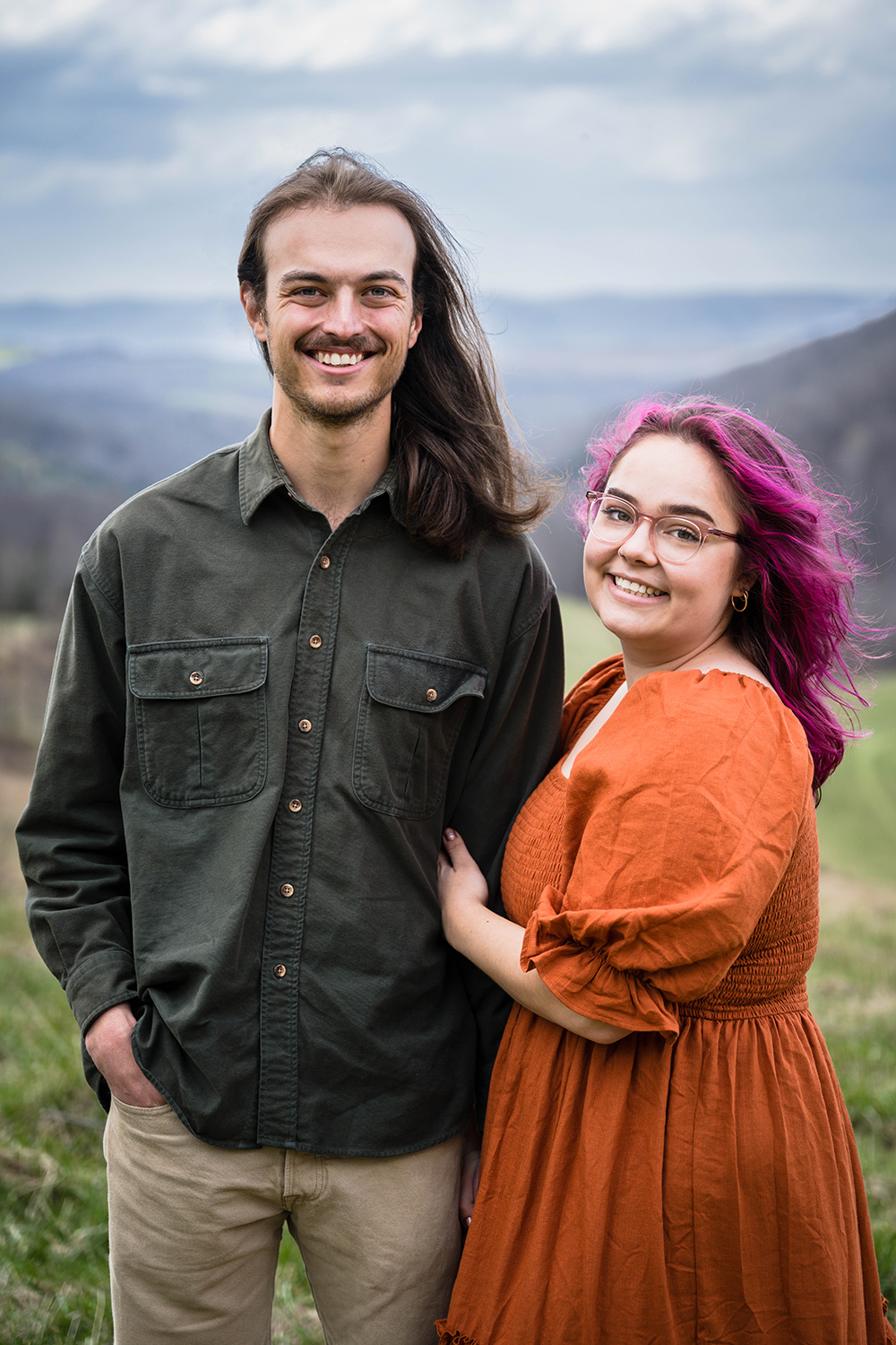 A couple wraps their arms around one another and smiles for a photo during their anniversary adventure session at Hidden Hills in Giles County, Virginia.