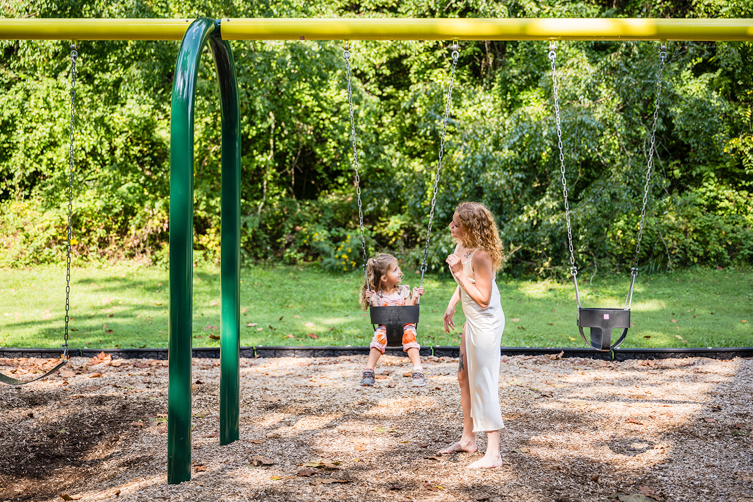 A marrier wearing a simple wedding dress pushes her daughter on the swing set at Fishburn Park in Roanoke, Virginia.