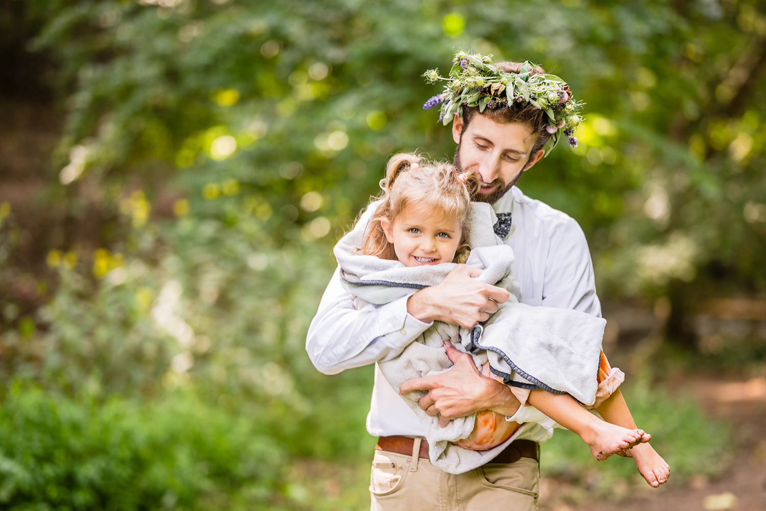 A marrier wearing a flower crown holds his daughter wrapped in a towel after playing in the water at FIshburn Park.