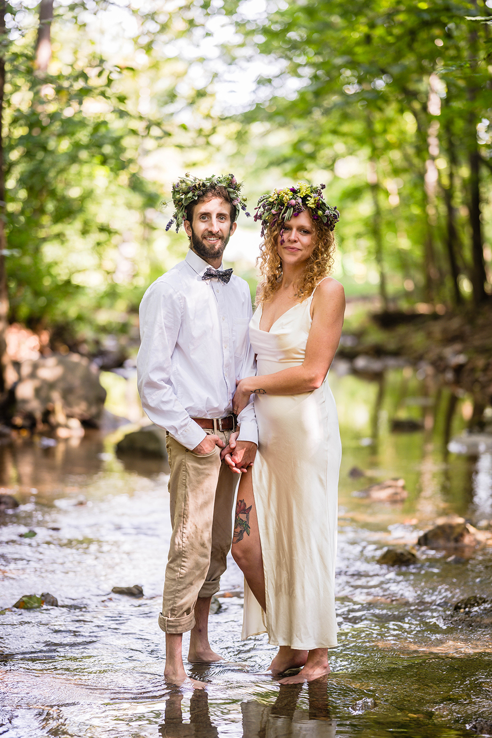 A couple holds hands and stands next to one another for a photo at Fishburn Park after their vow renewal ceremony. The pair stands in the shallow creek barefoot and smiles for a photo together. 