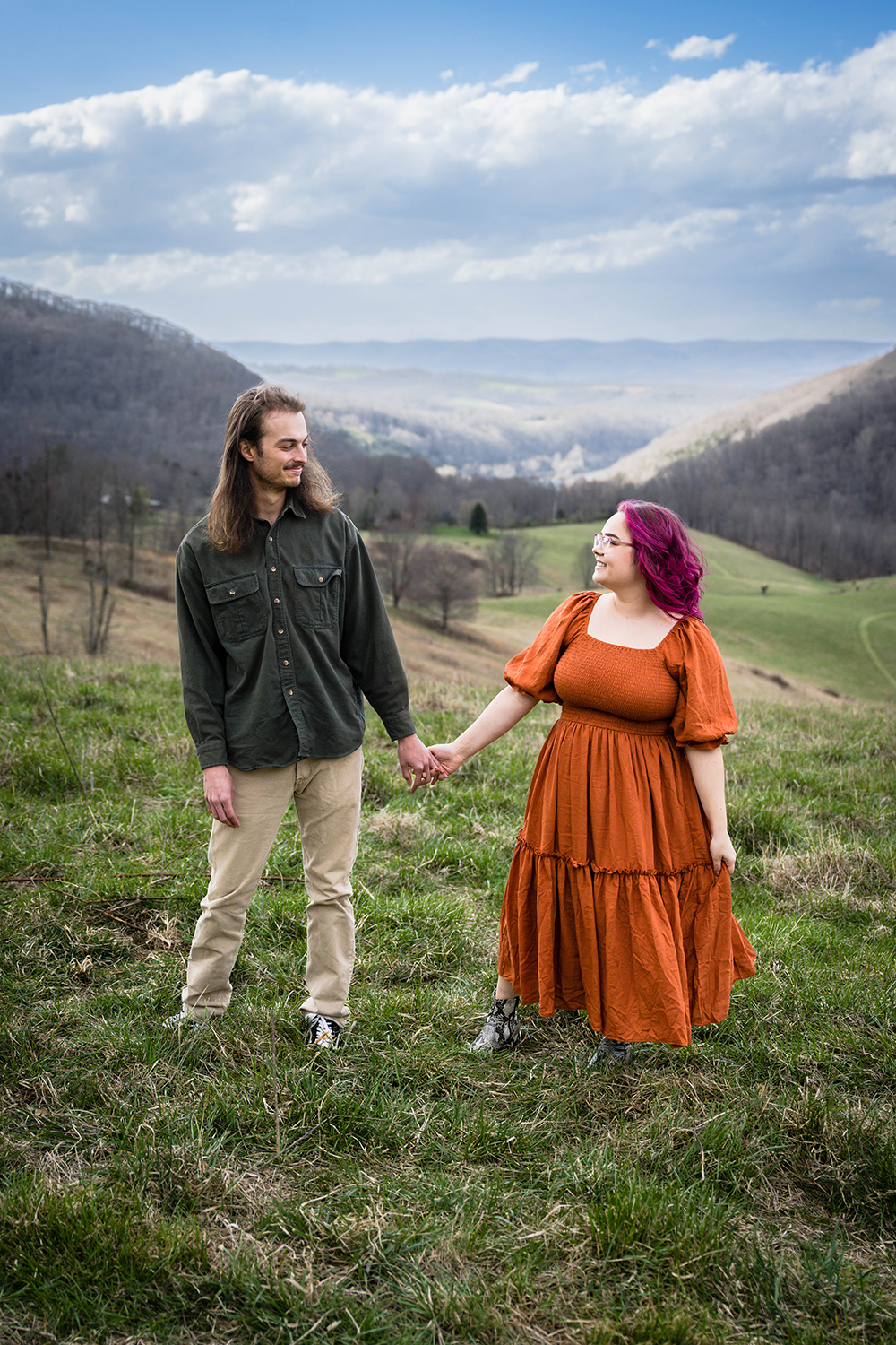 A couple holds hands and looks at one another atop of a hill overlooking the Blue Ridge Mountains in Giles County, Virginia.