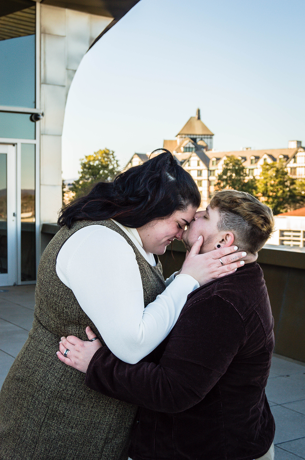 A trans man kisses the forehead of his partner on the balcony of the Taubman Museum of Art for their couples adventure session.