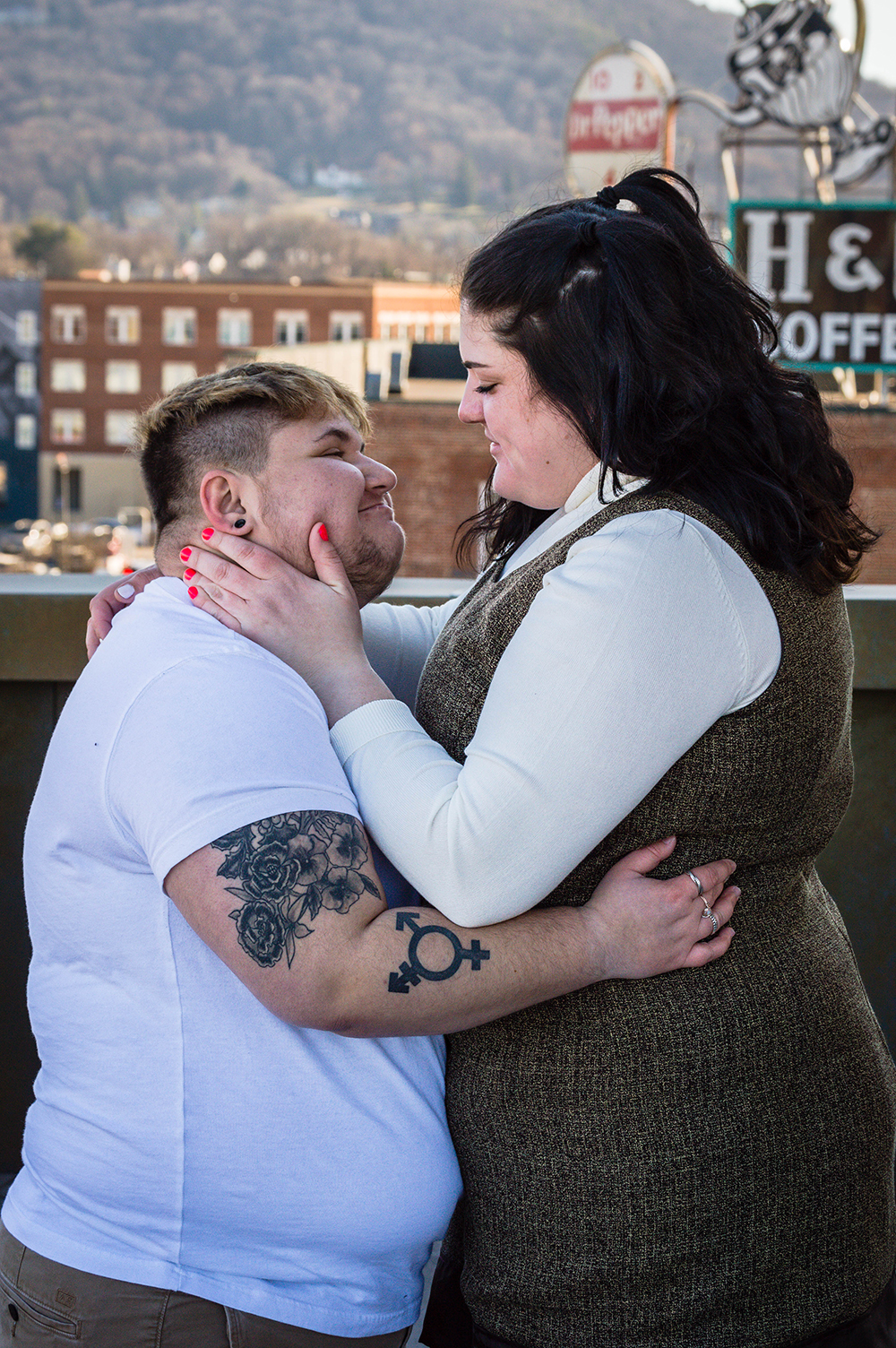 A couple holds onto one another and looks lovingly at one another on the balcony of the Taubman Museum of Art for their couples adventure session.