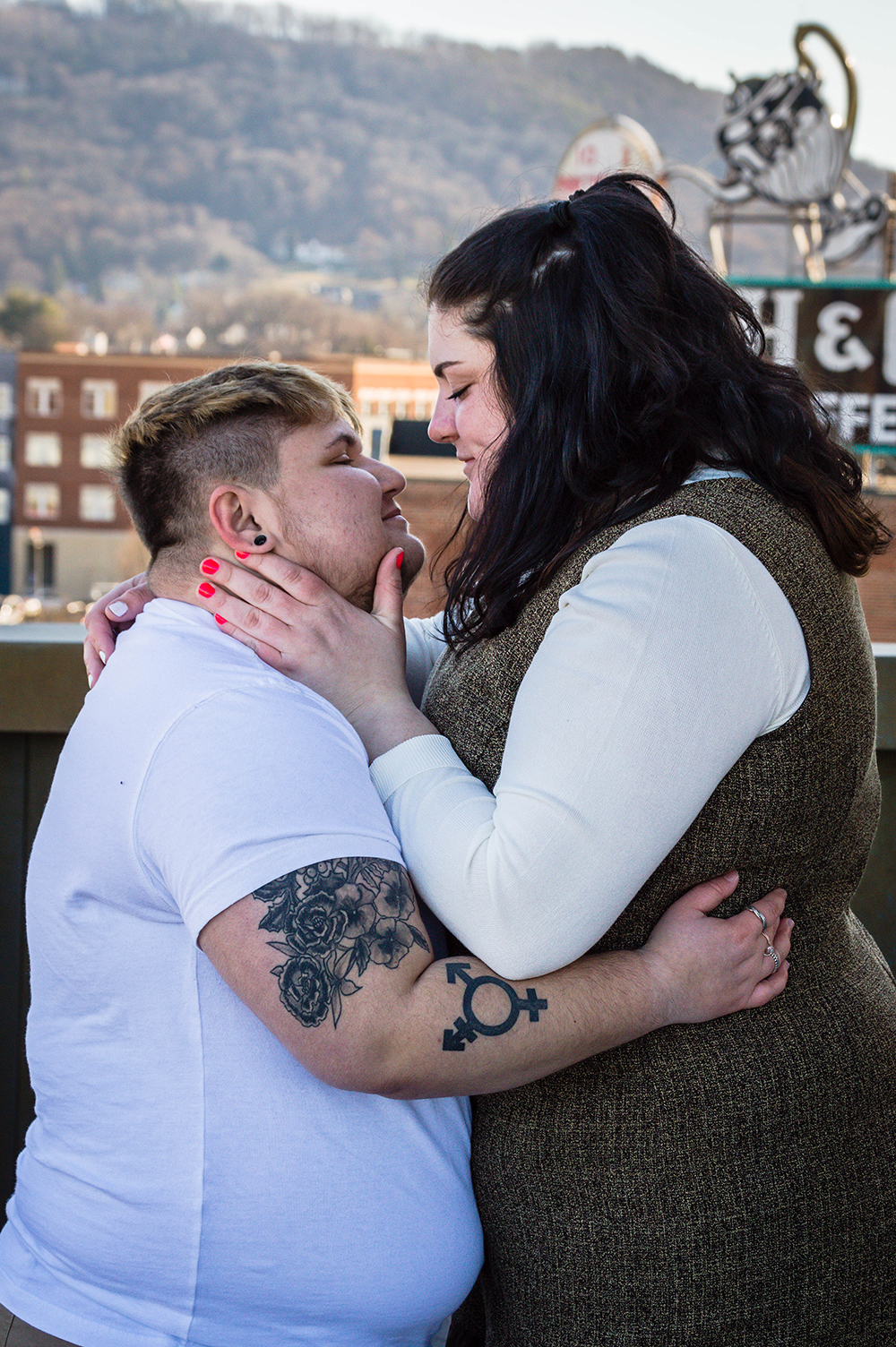 A couple holds onto one another and looks lovingly at one another on the balcony of the Taubman Museum of Art for their couples adventure session.