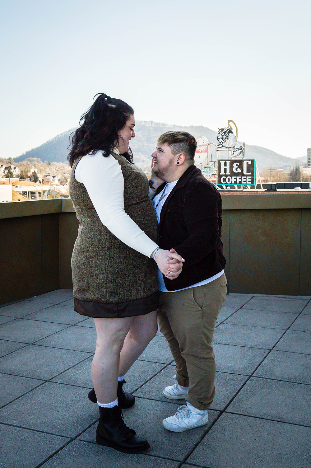 An LGBTQ+ couple dances together while looking lovingly at one another on the balcony of the Taubman Museum of Art for their couples adventure session.