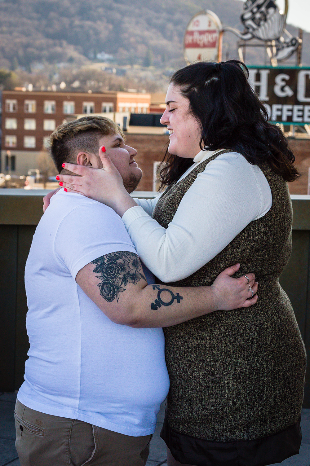 An LGBTQ+ couple holds onto one another and looks lovingly at one another on the balcony of the Taubman Museum of Art for their couples adventure session.