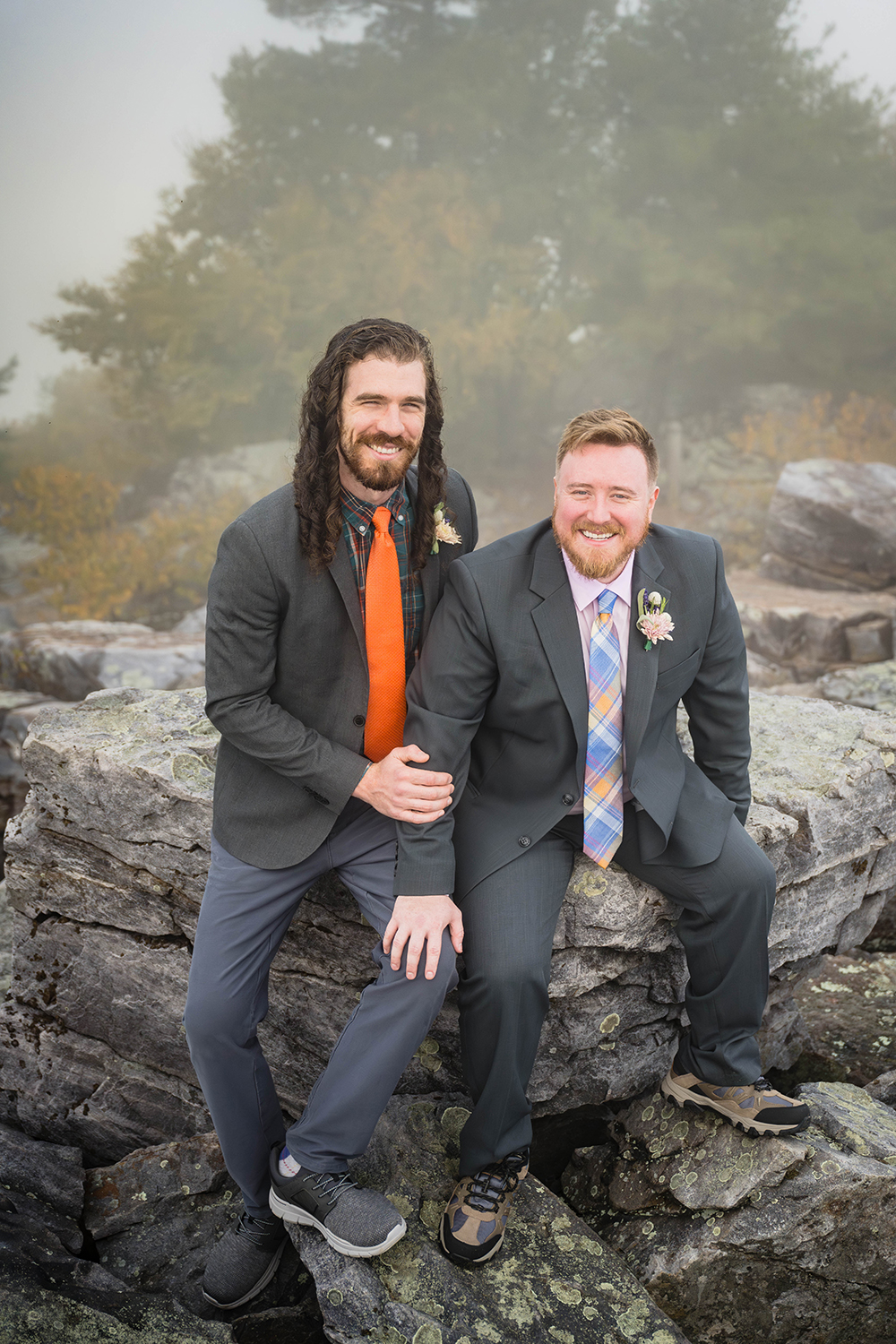 A queer couple sits on a rock together with trees in the background at Blackrock Summit.