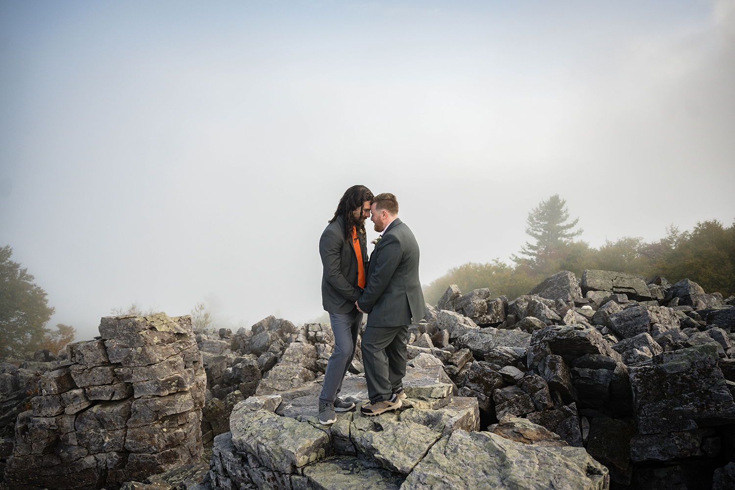 A gay couple stand in front of one another while resting their foreheads together and holding hands with their eyes closed atop Blackrock Summit for a "quiet moment" during their ceremony. 