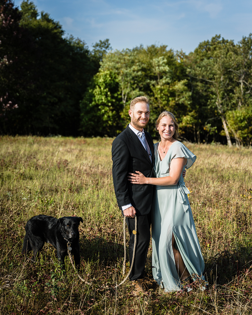 A newlywed couple smile together with their dog in a field at Tanners Ridge Overlook in Shenandoah National Park.