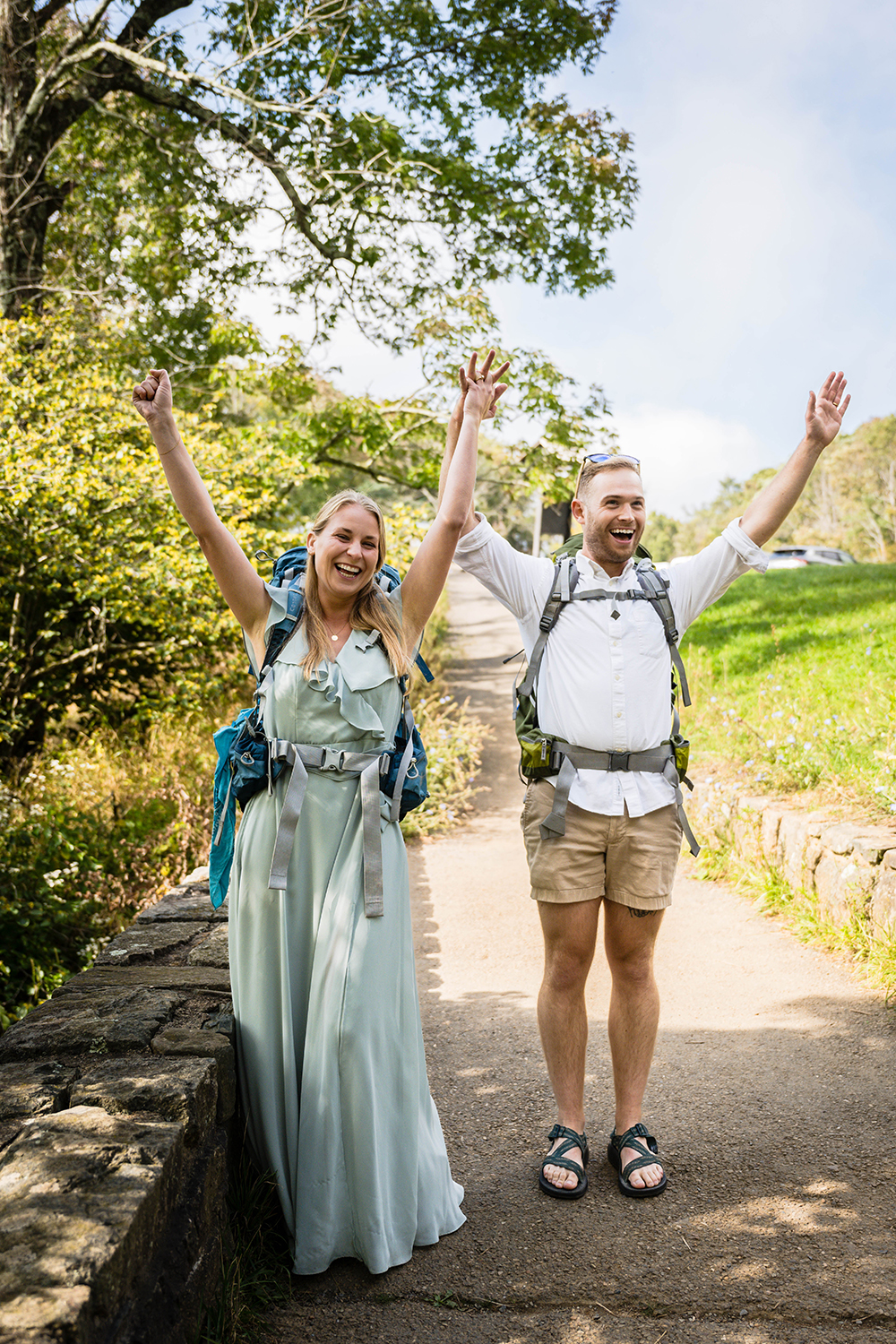 A couple on their elopement day raises their arms in excitement before they begin their hike to Dark Hallow Falls in Shenandoah National Park.