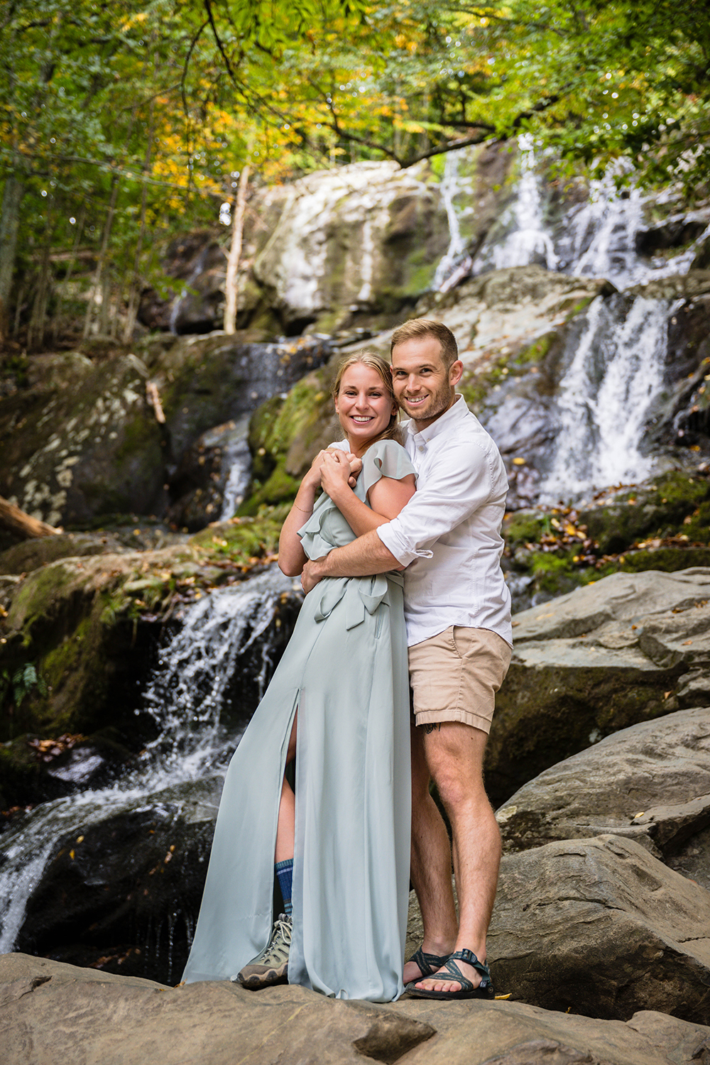 A couple on their elopement day embrace as they stand on top of a large rock in front of Dark Hallow Falls in Shenandoah National Park.