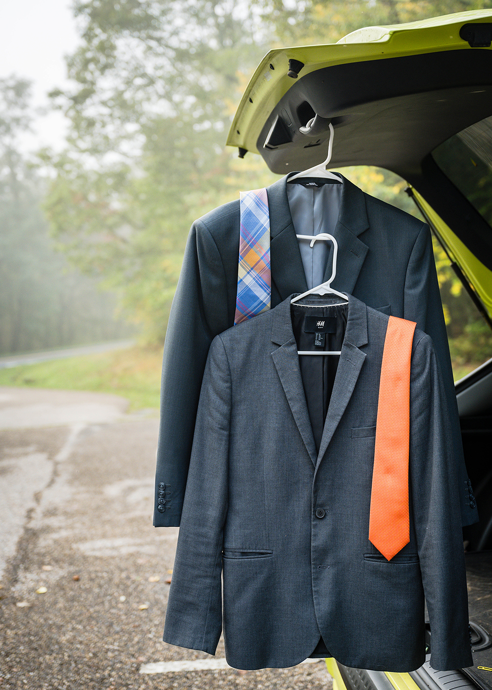 Two suit jackets and ties neatly hanging from the trunk of a car,