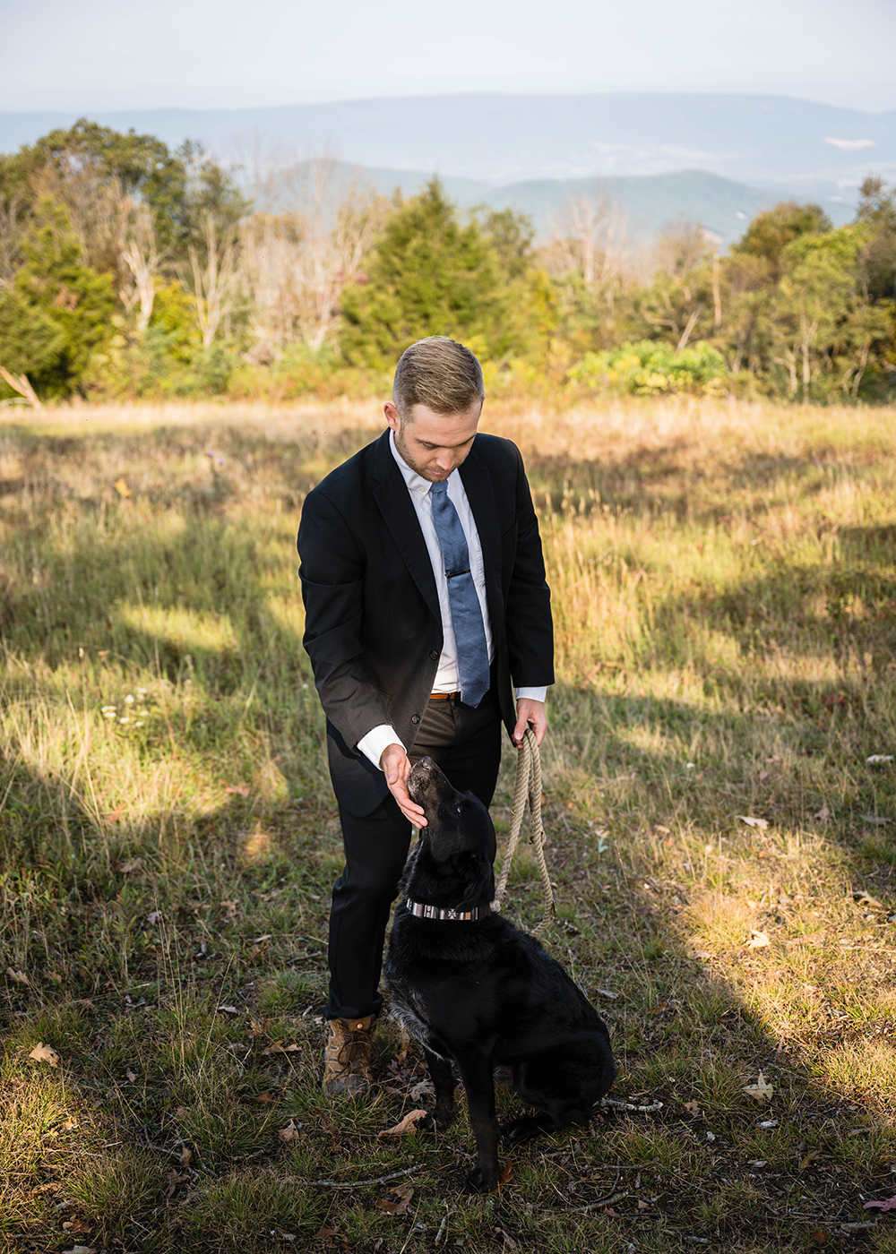 A groom scratches the chin of his dog in a meadow at Tanner's Ridge Overlook.