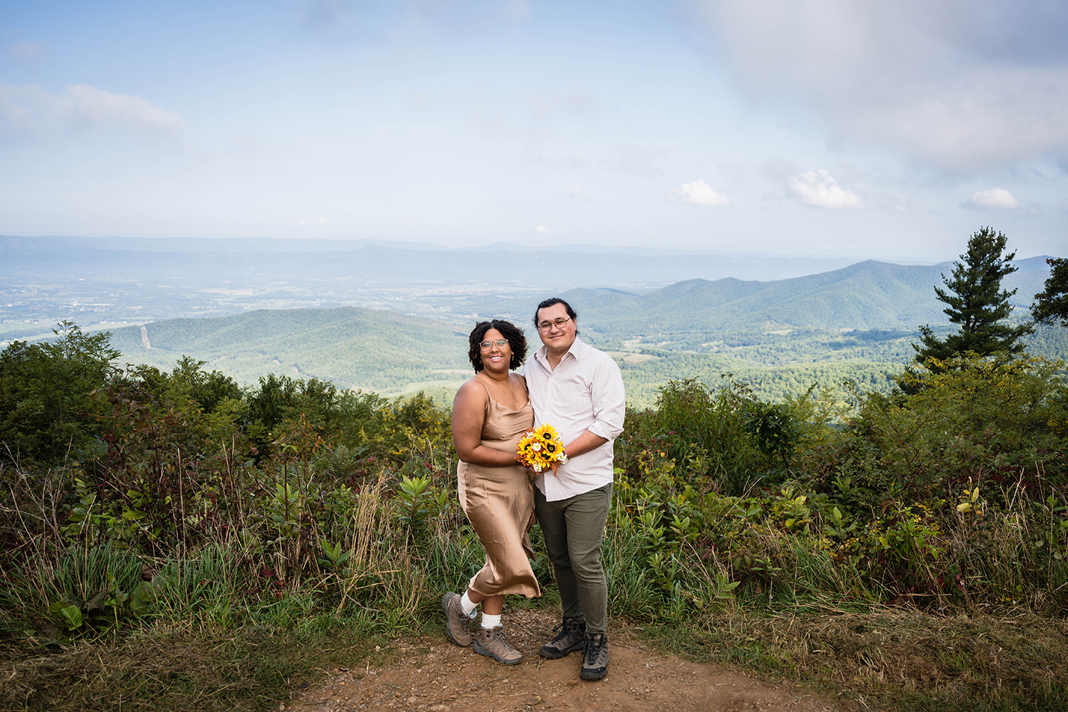 A couple stands together for a photo at Jewell Hollow Overlook, which features a beautiful view of the Blue Ridge Mountains,