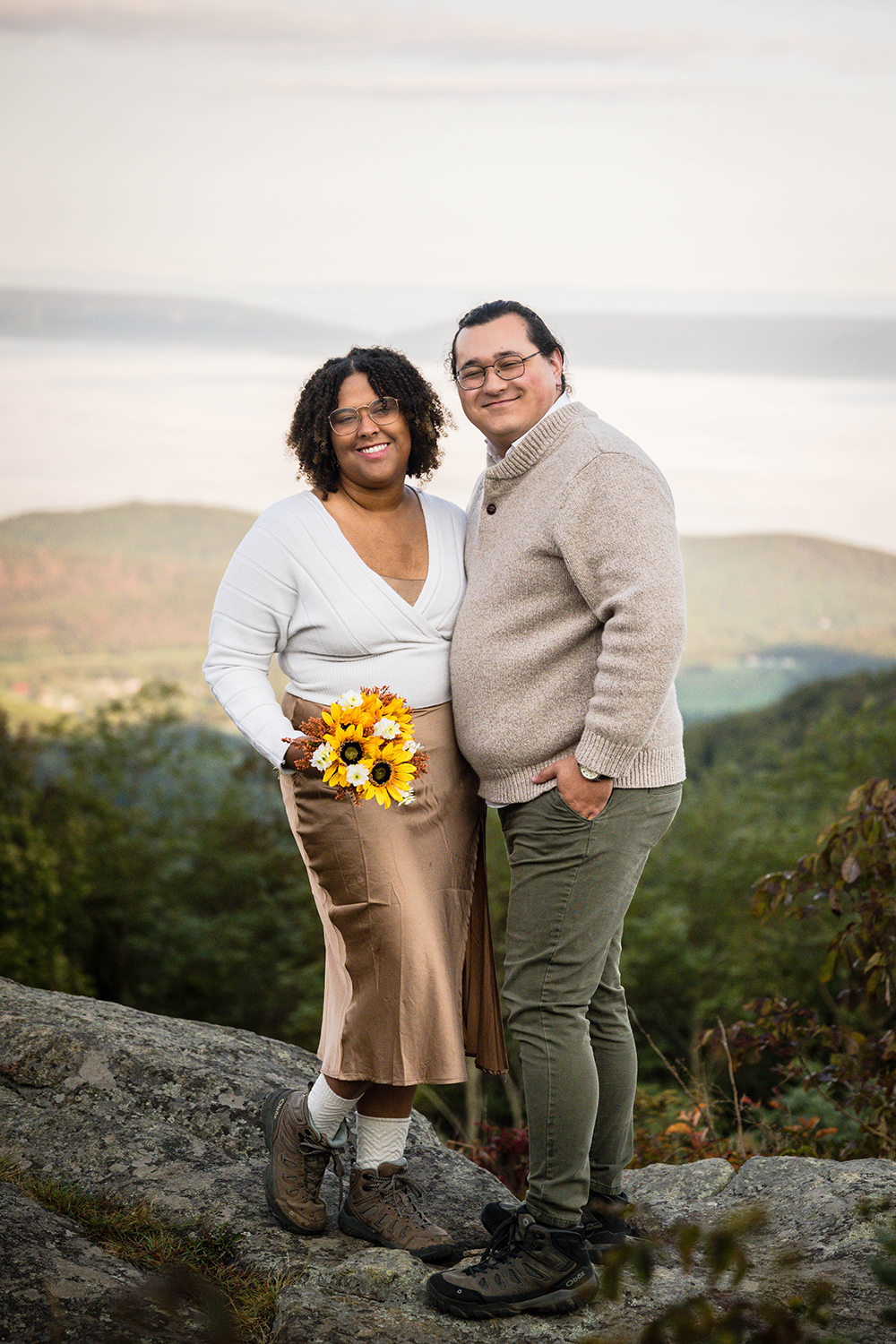 An elopement couple stand together on a large rock at Timber Hollow Overlook and smile for one of their first photos as newlyweds.