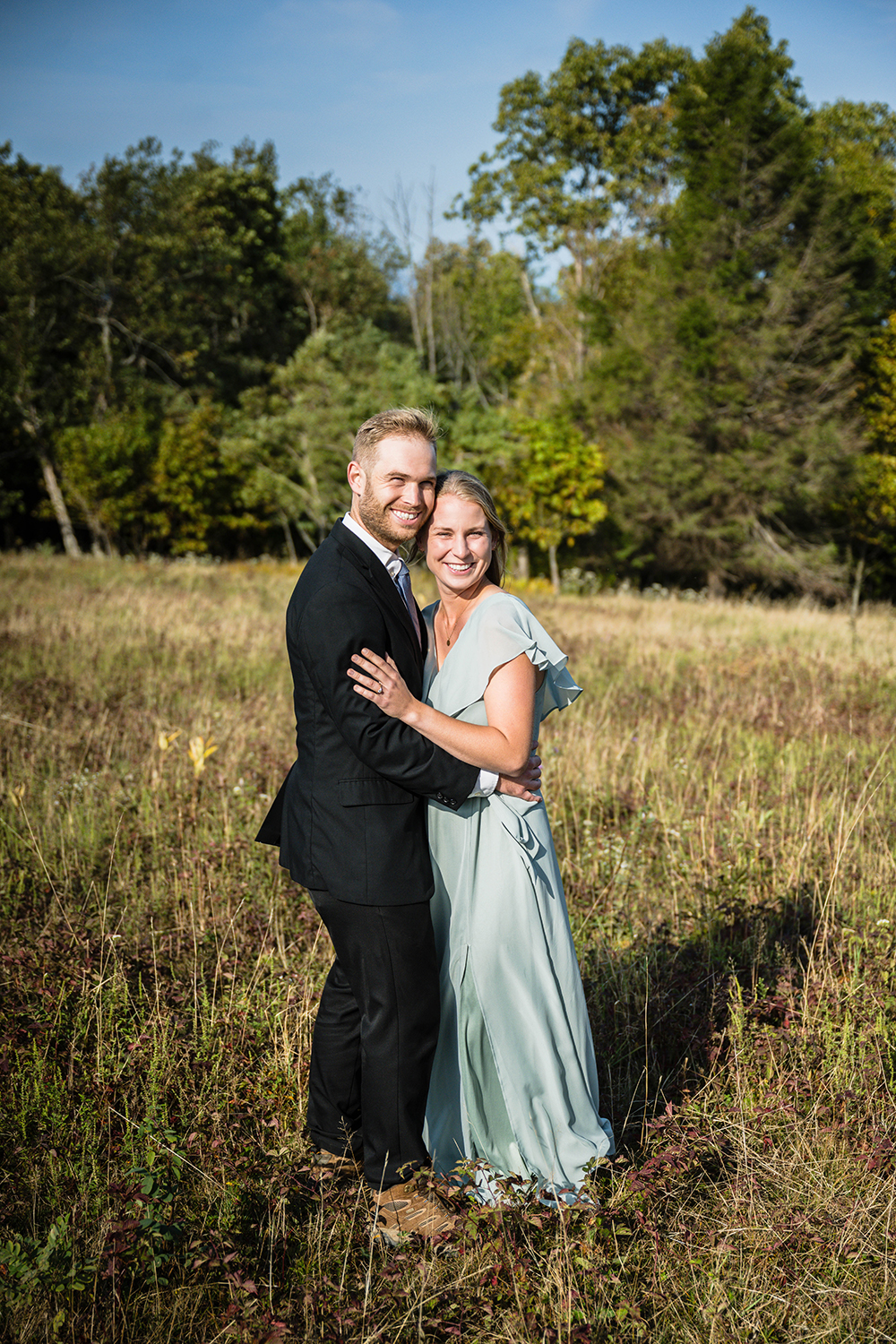 A newlywed couple smile together in a field at Tanners Ridge Overlook in Shenandoah National Park.