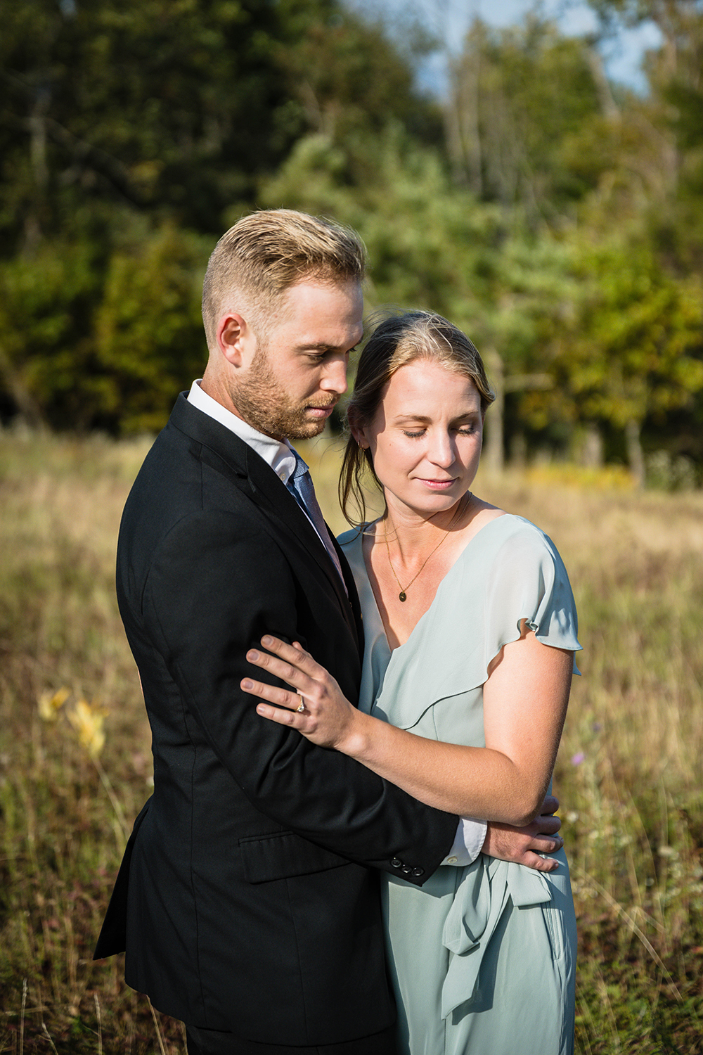 A newlywed couple holds onto one another with their eyes closed and serious expressions as they stand in a field at Tanners Ridge Overlook in Shenandoah National Park.