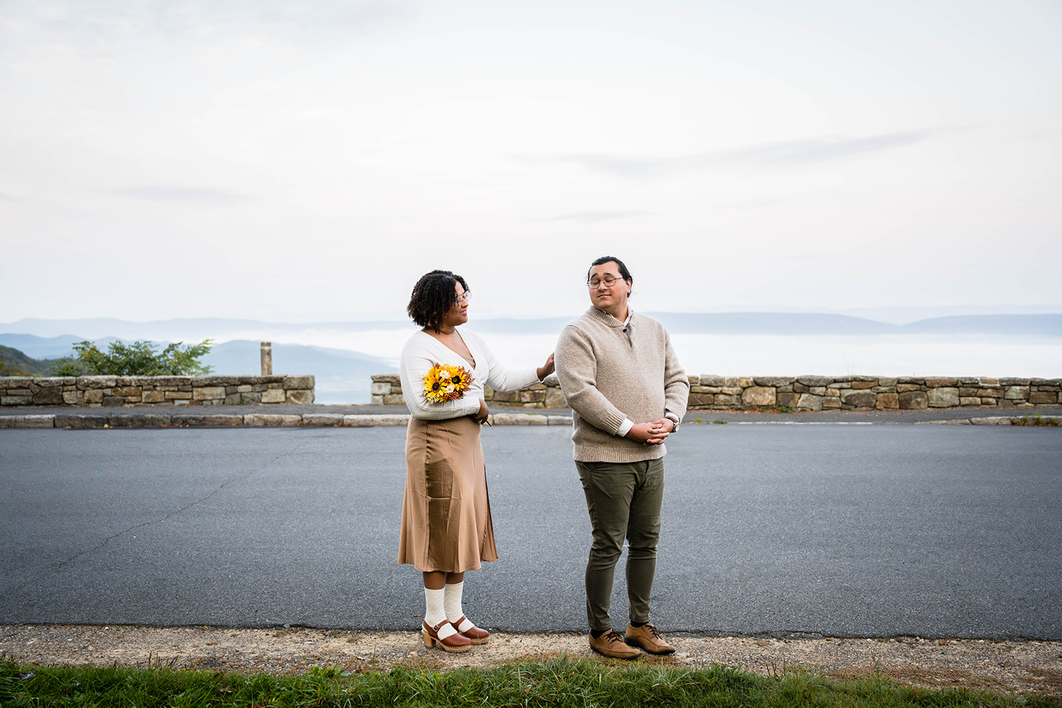 A bride taps the shoulder of her soon-to-be husband during their first look. Both of their eyes are closed and the groom turns towards his soon-to-be wife with his hands in front of him. 