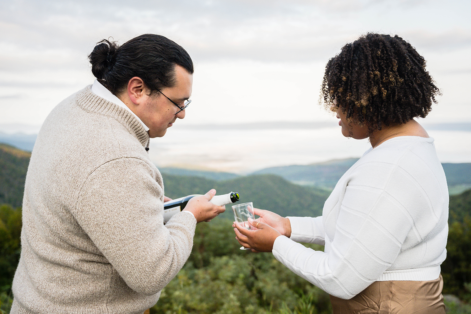 A bride holds a glass to her groom who then pours sparkling cider in it for their wedding ceremony.