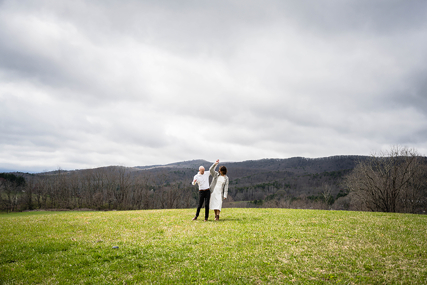  A couple in wedding attire stands in a vibrant field, with breathtaking mountains providing a picturesque backdrop.