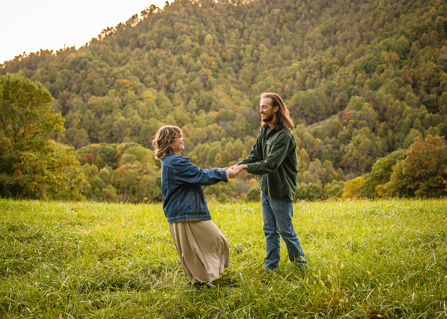 A couple holds each other's hands and begins to spin around in a circle together on a mountain during their fall engagement session.