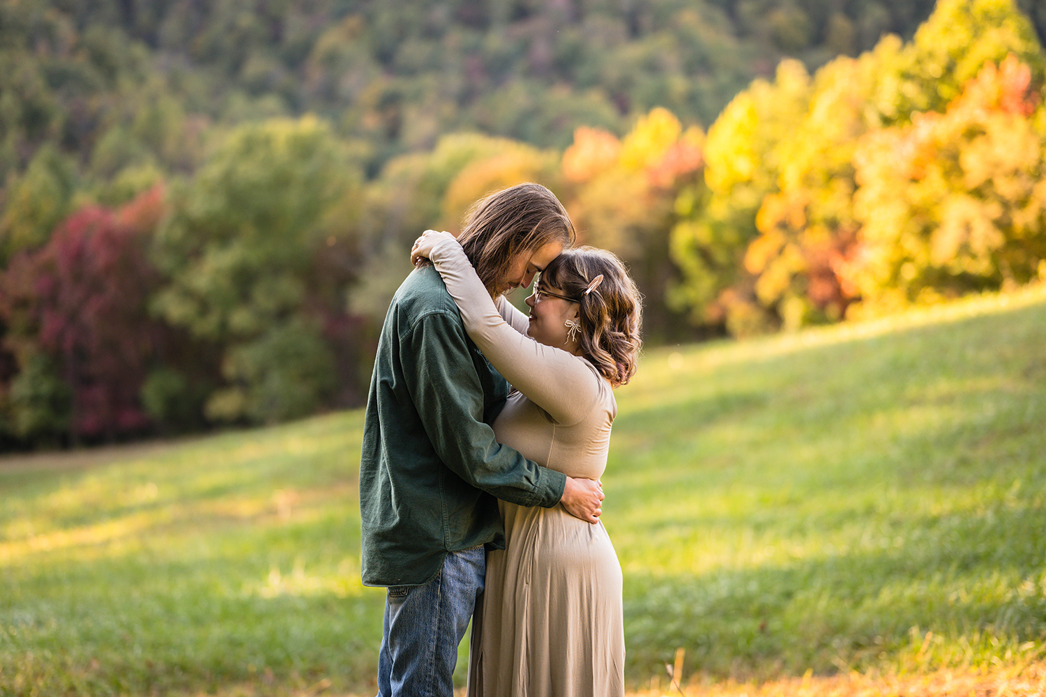 A couple during their fall engagement photoshoot faces one another and wraps their arms around each other. The man wraps his arms around the woman's waist while the woman wraps her arms around the man's neck.