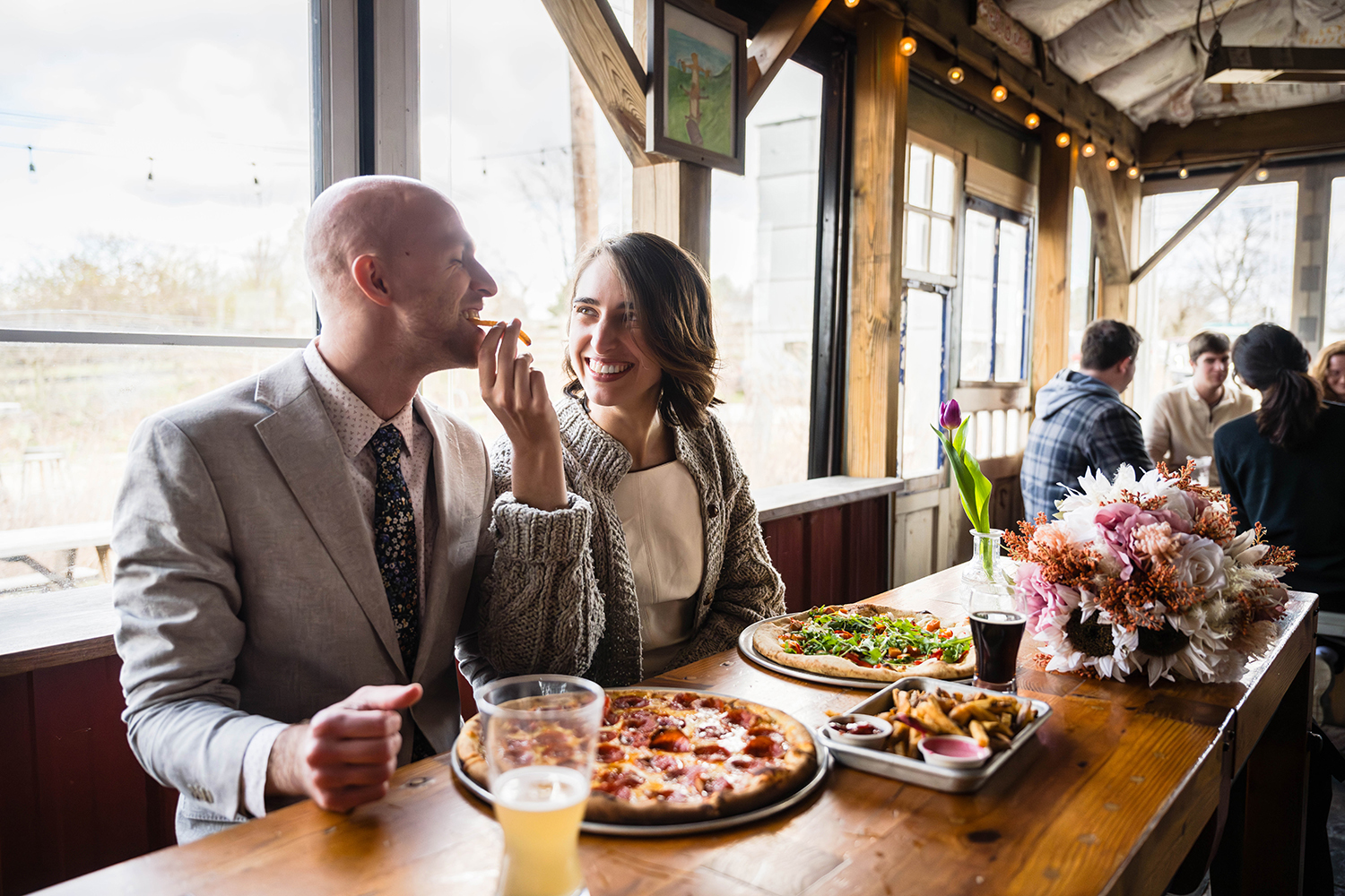 A couple seated at a restaurant, happily sharing a pizza, surrounded by a warm and inviting atmosphere on their elopement day in Virginia.